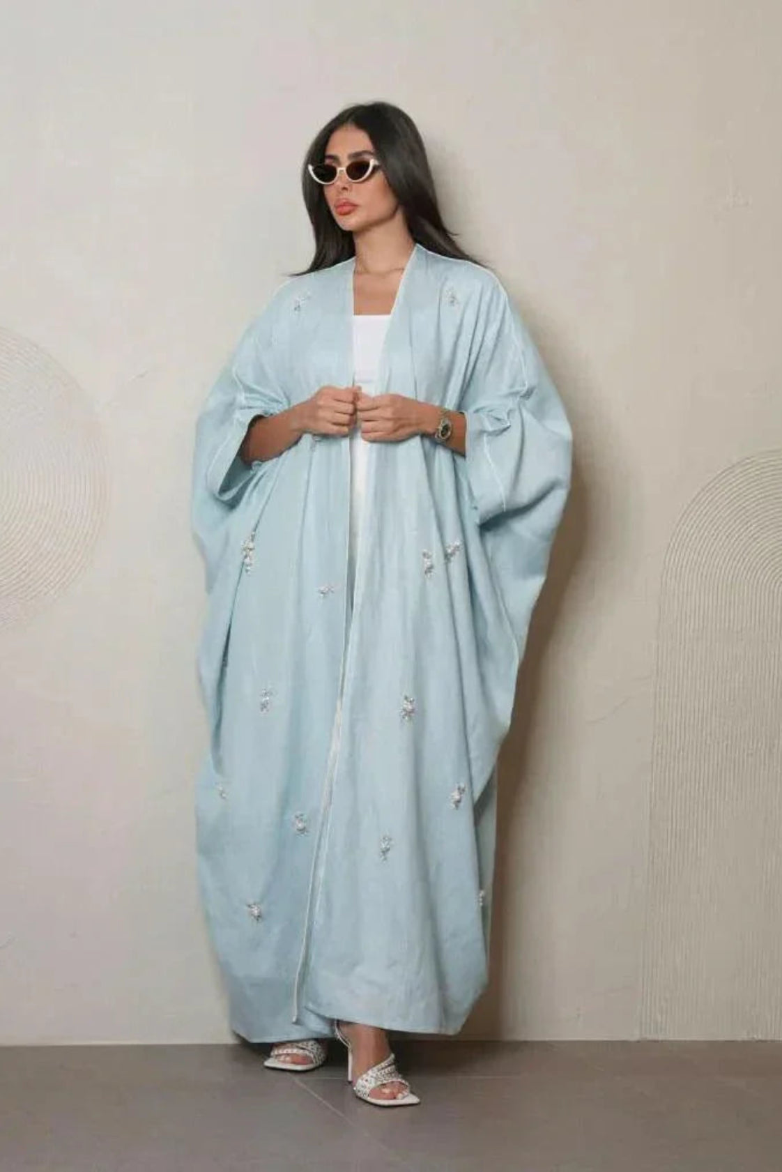 Woman wearing a sky-blue lightweight linen abaya with delicate white and crystal hand embroidery, styled with white sandals and sunglasses.
