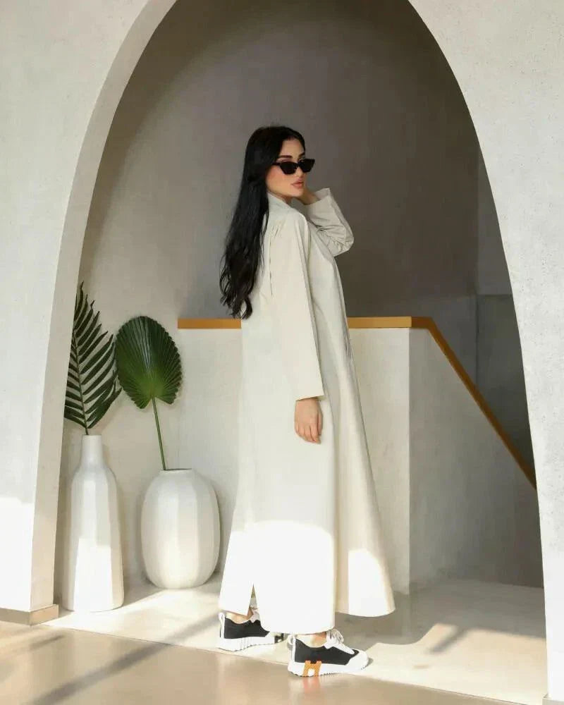 Cream blazer-style abaya with double-breasted black buttons and side pockets, tailored in structured crepe fabric for a modern classic look.