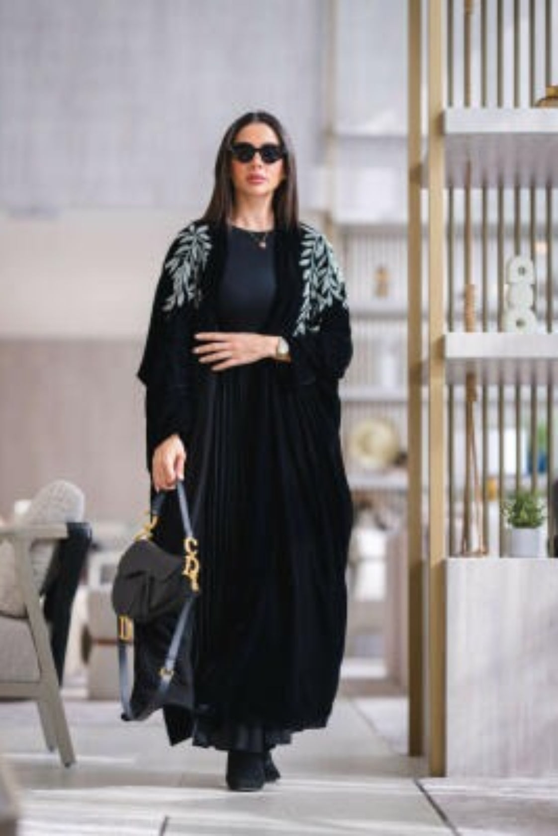 Woman wearing a luxurious black velvet abaya with silver leaf embroidery on shoulders and sleeves, styled with sunglasses and a black handbag.