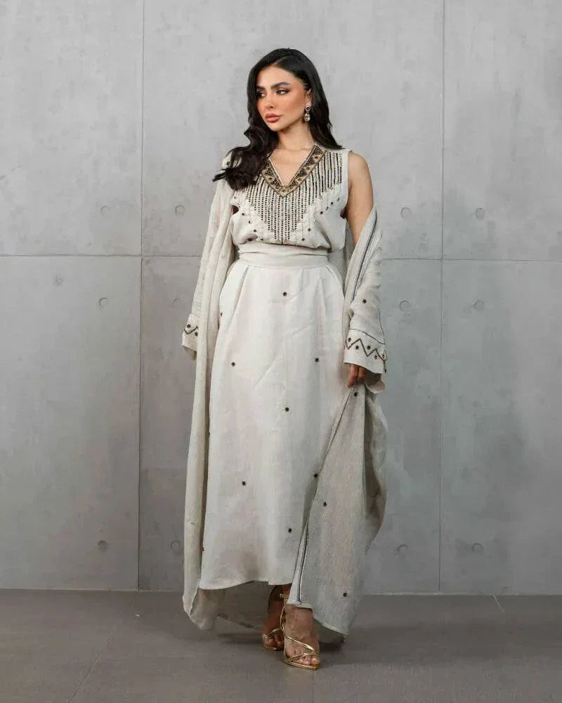 Woman wearing a beige three-piece linen set with sleeveless embroidered top, high-waisted skirt, and matching shawl with stitched accents.