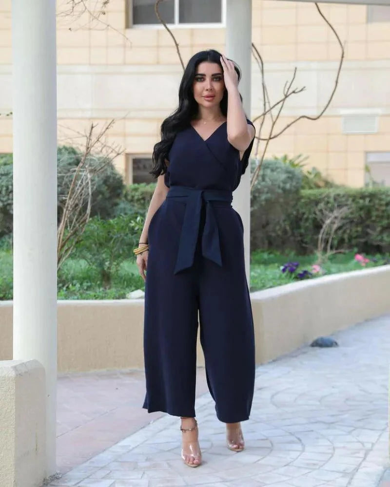 Woman wearing a navy blue crepe jumpsuit with V-neckline, waist tie, and wide-leg trousers standing outdoors