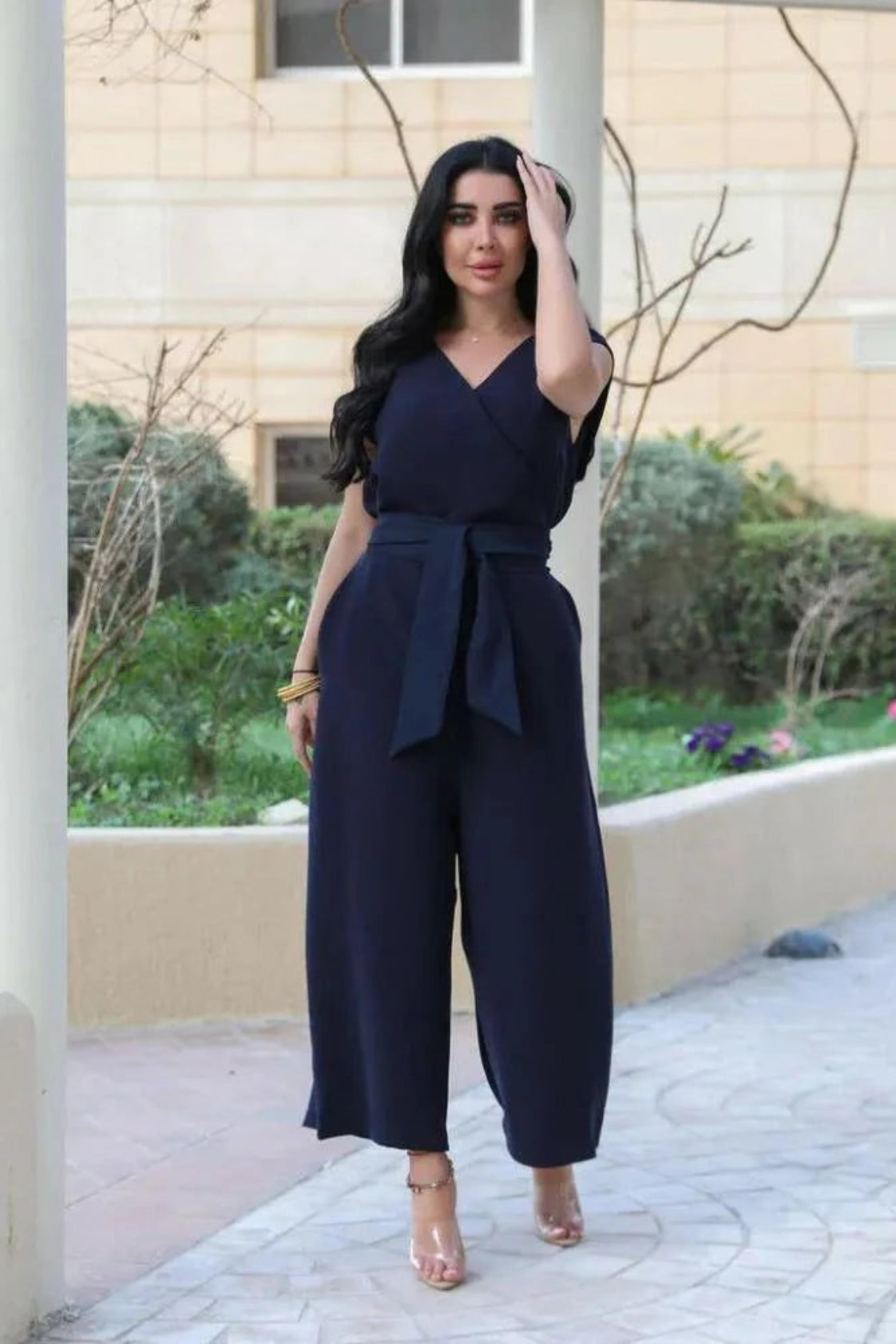 Woman wearing a navy blue crepe jumpsuit with V-neckline, waist tie, and wide-leg trousers standing outdoors