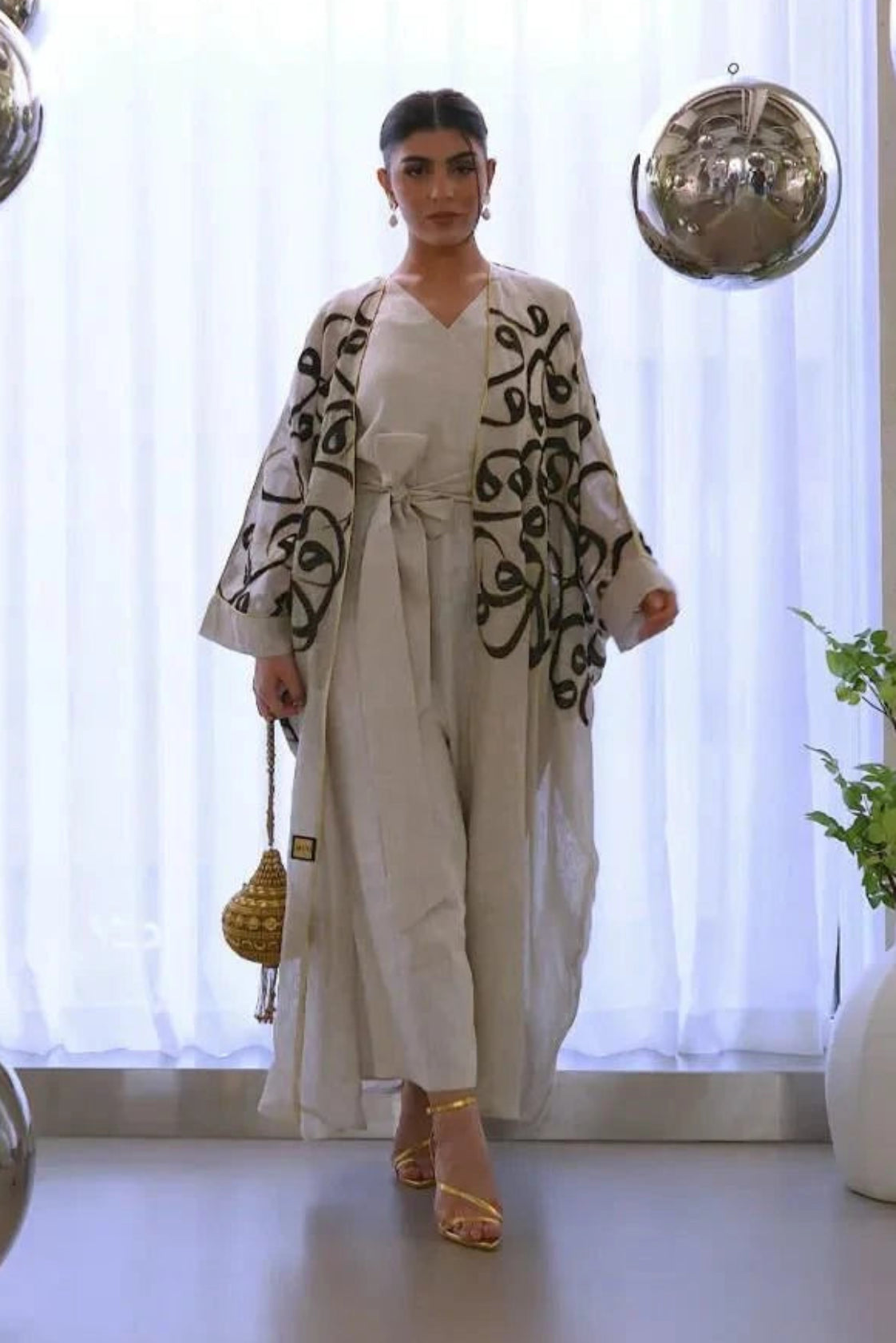 woman wearing natural beige statement linen bisht with bold black calligraphy embroidery in modern elegant setting