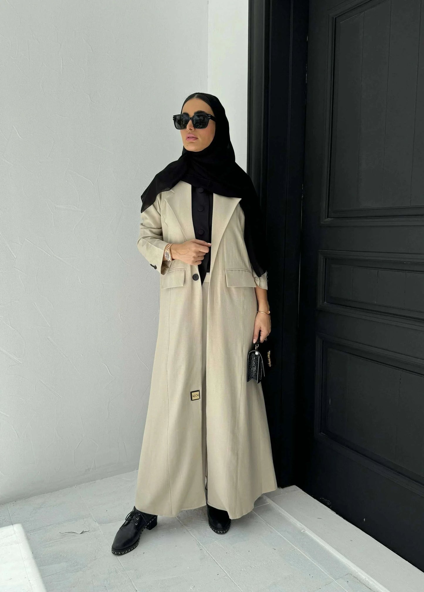 Woman wearing beige linen blazer-style abaya with lapel collar, single-button closure, front flap pockets, and turned-up cuffs.