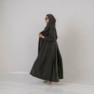 Woman wearing an olive green lightweight abaya made of cobra silk with soft cloche cut and back pleats, accessorized with sunglasses and a handbag.