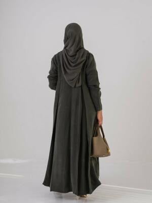 Woman wearing an olive green lightweight abaya made of cobra silk with soft cloche cut and back pleats, accessorized with sunglasses and a handbag.