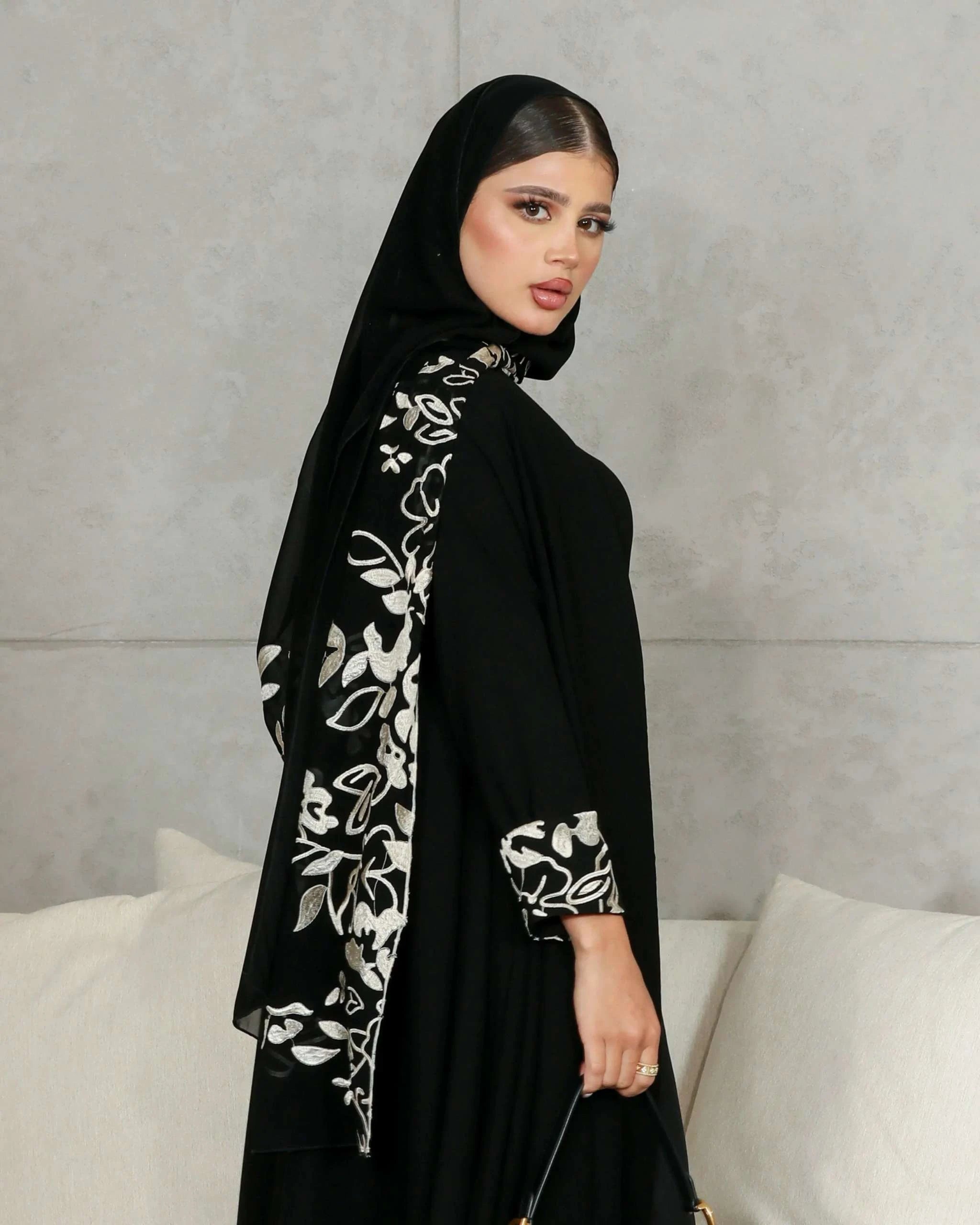 Woman wearing elegant black crepe abaya with embroidered scarf detailing on sleeves and back.