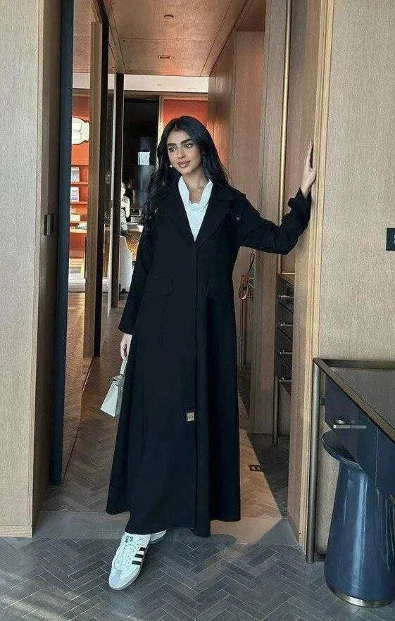 woman wearing black blazer-style abaya with button detailing on shoulders and back holding beige handbag