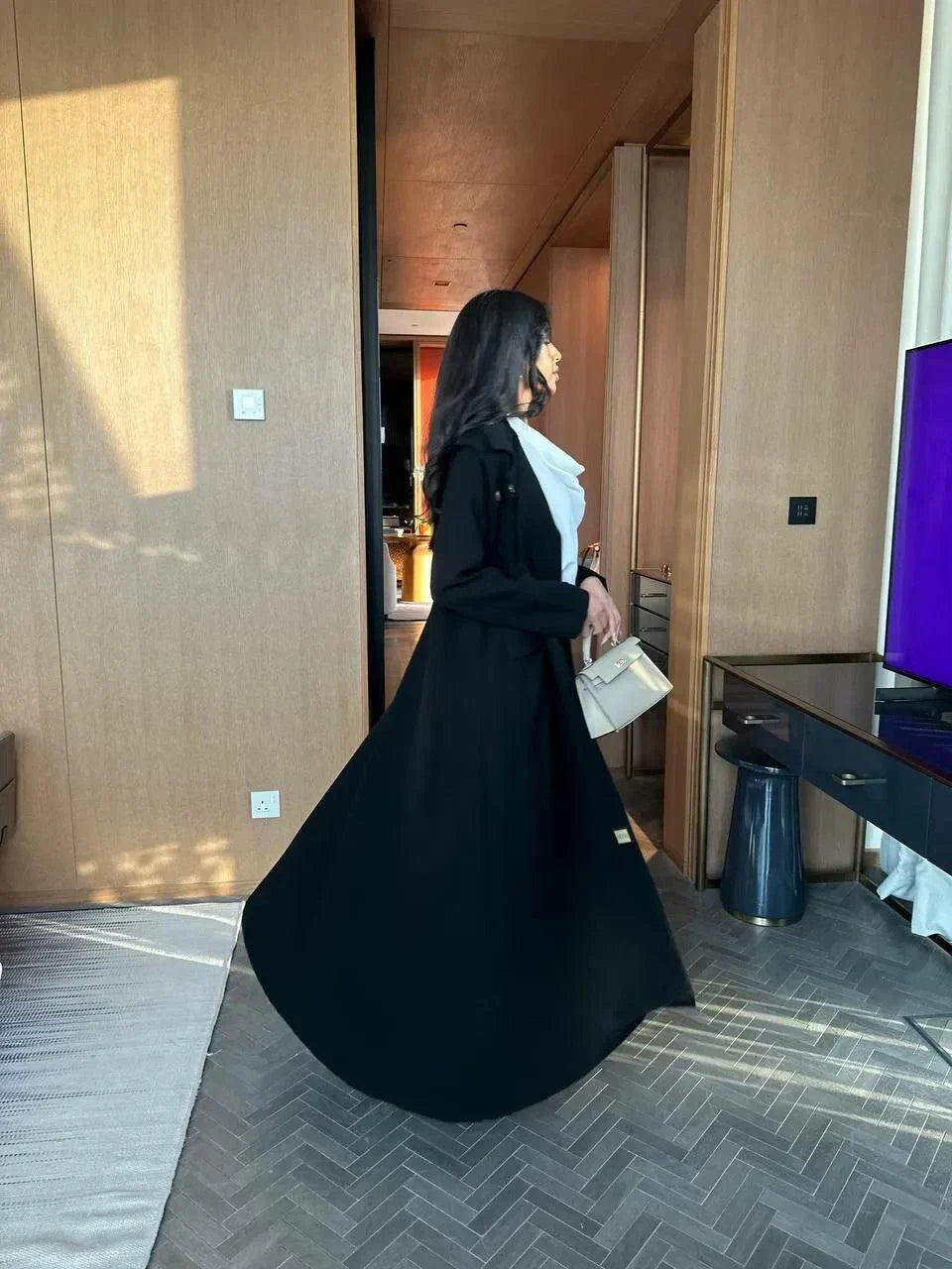 woman wearing black blazer-style abaya with button detailing on shoulders and back holding beige handbag
