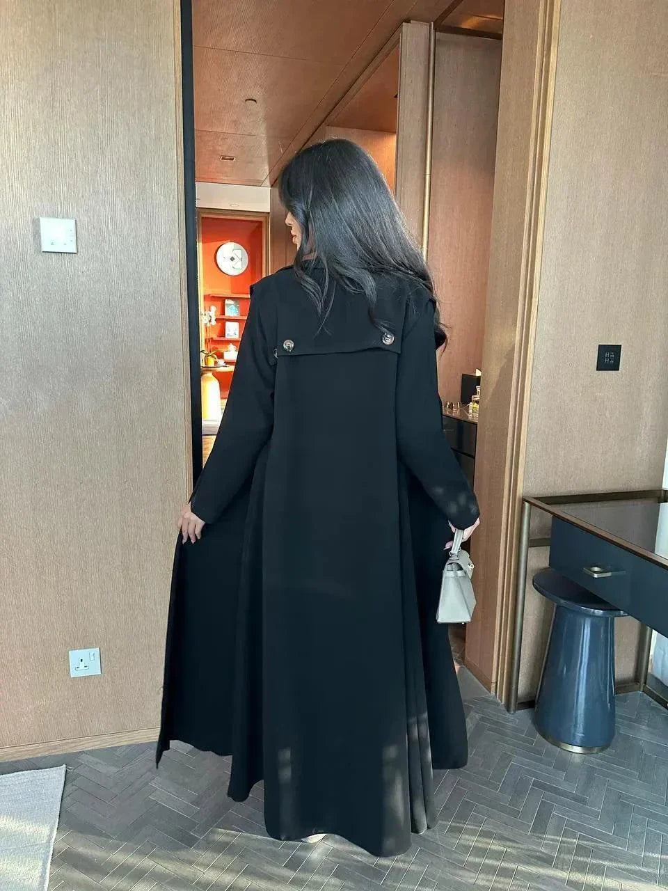 woman wearing black blazer-style abaya with button detailing on shoulders and back holding beige handbag