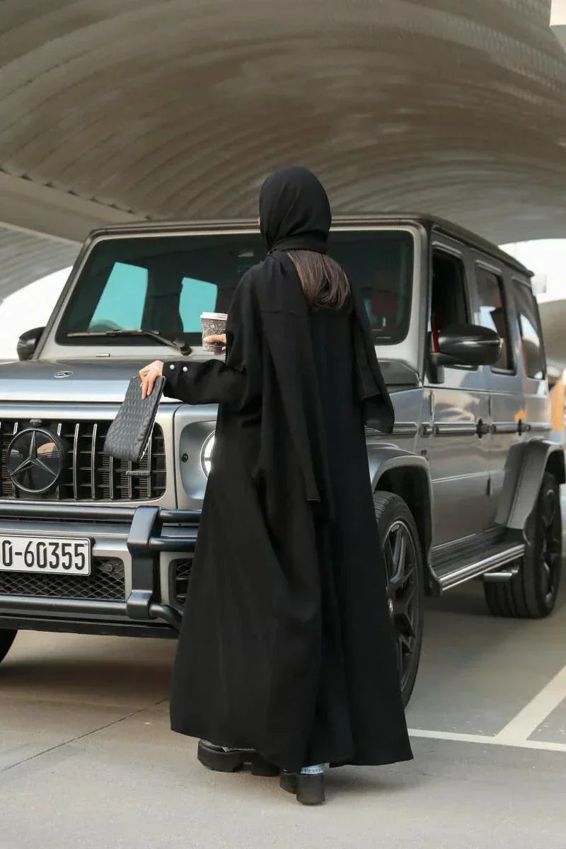 woman wearing classic black abaya with soft crepe fabric draped elegantly outdoors near car