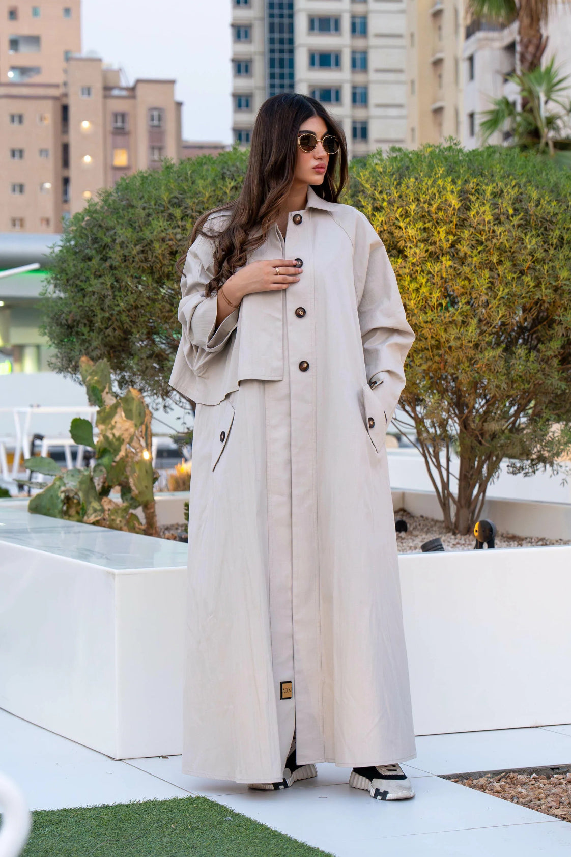 Woman wearing beige Sandline free-size trench coat with front buttons and flap pockets outdoors