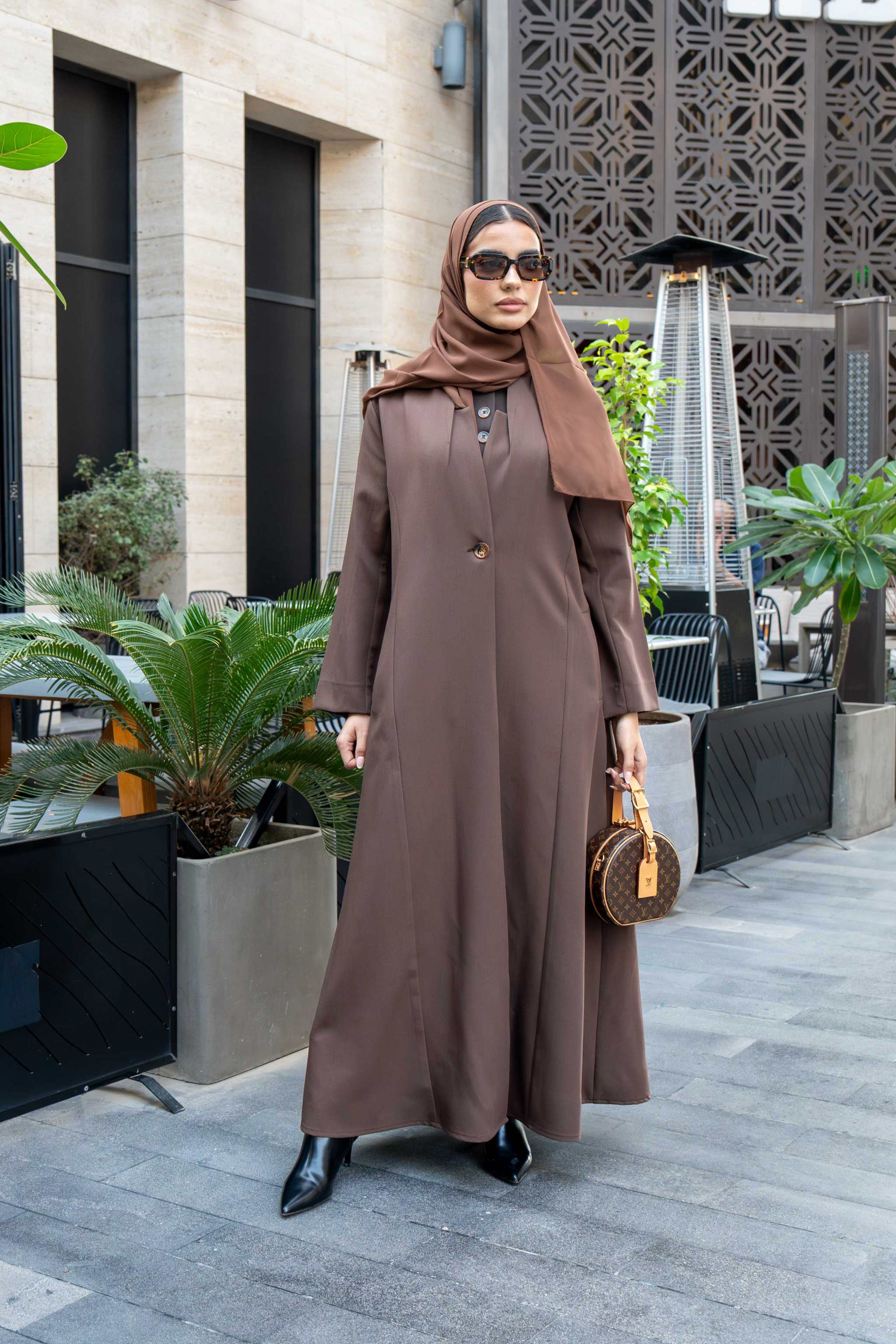 woman wearing classic brown crepe abaya with hijab and sunglasses outdoors carrying a small handbag