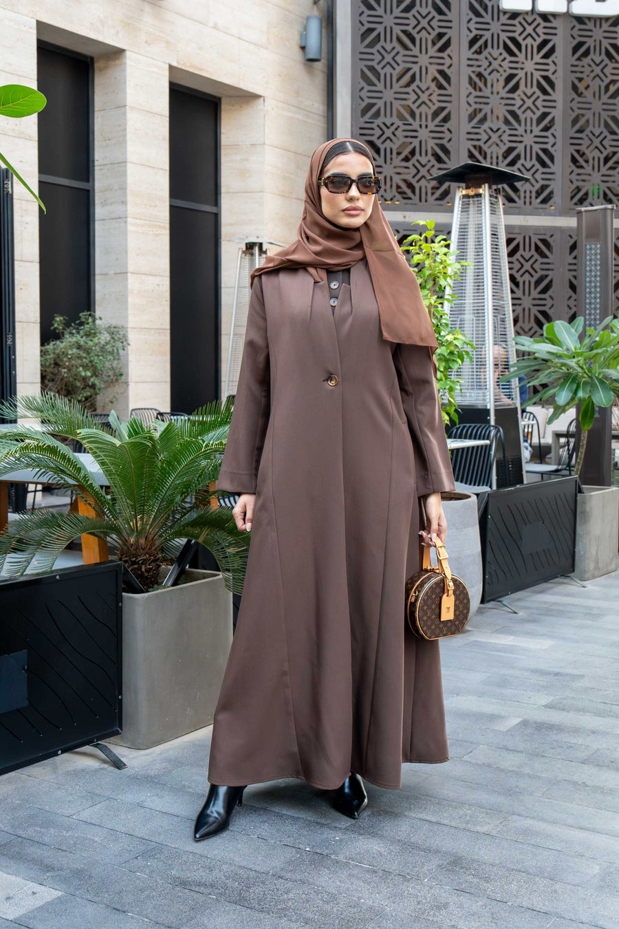 woman wearing classic brown crepe abaya with hijab and sunglasses outdoors carrying a small handbag