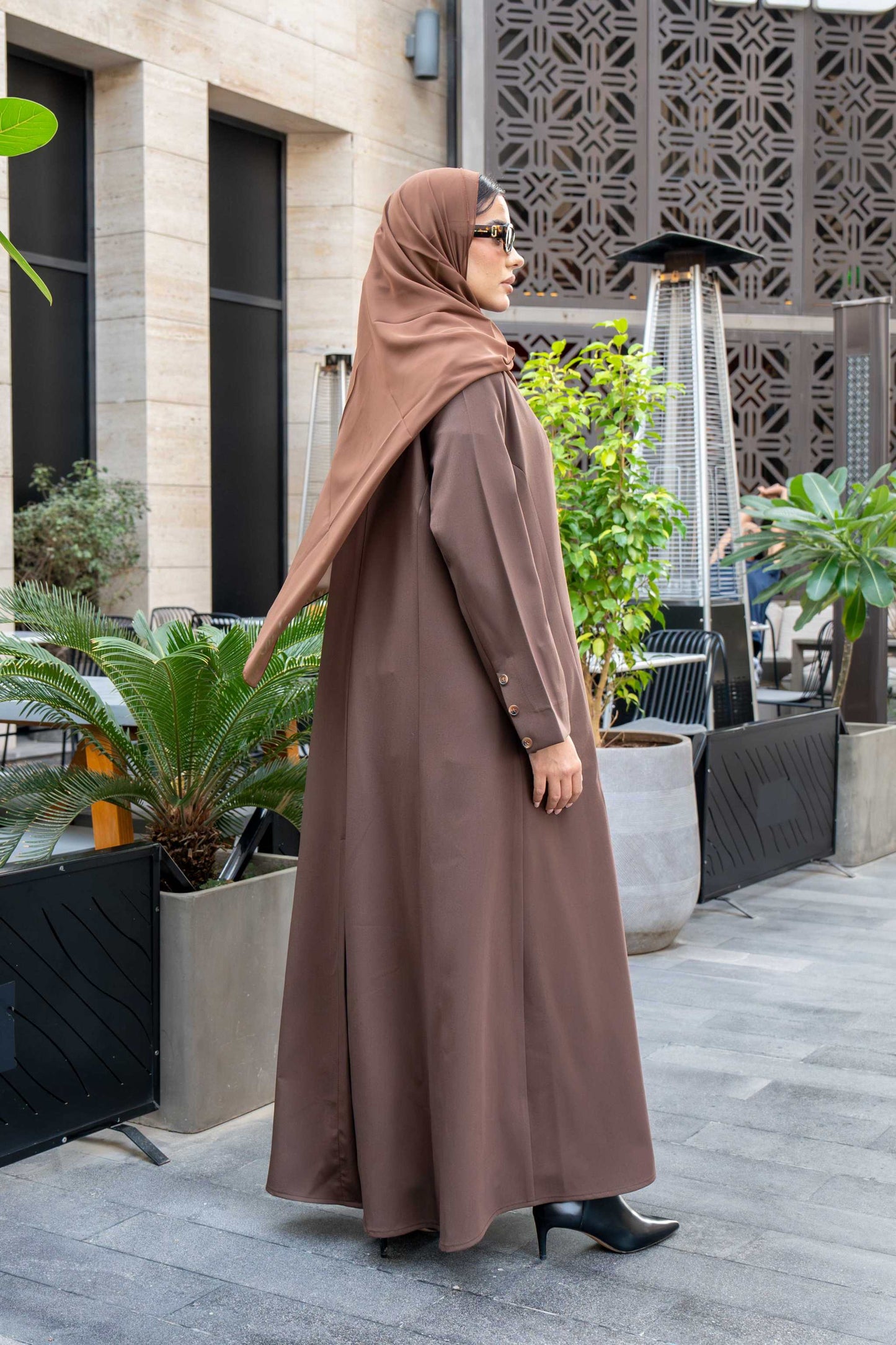Woman wearing classic brown crepe abaya with hijab and sunglasses outdoors