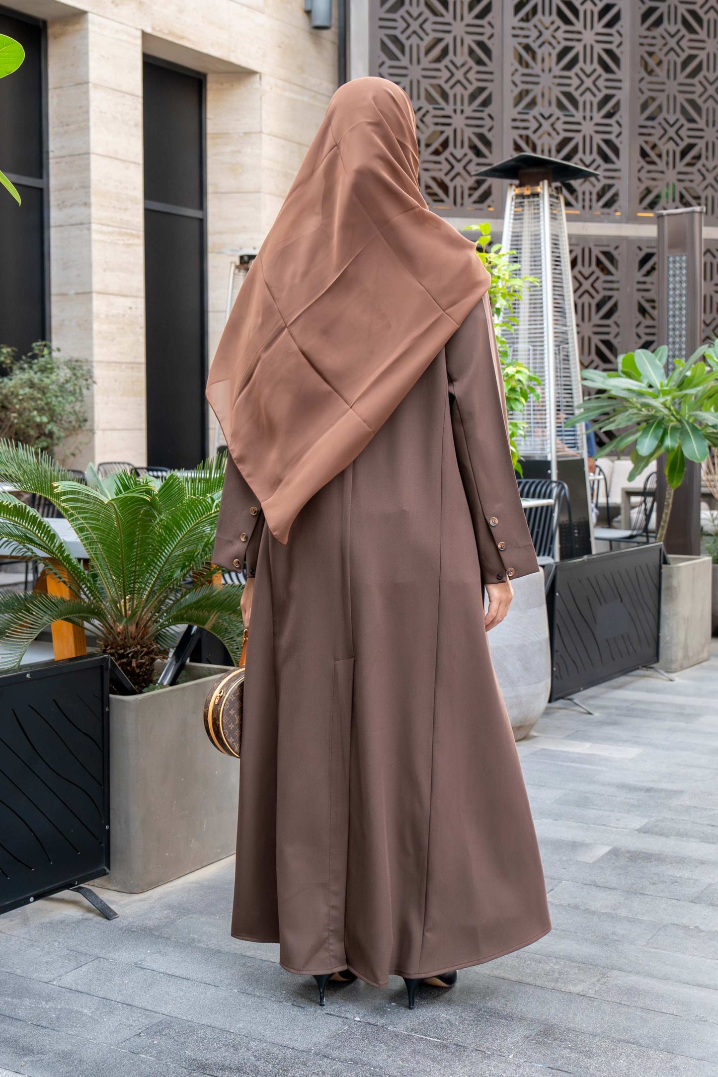 Woman wearing classic brown crepe abaya with hijab and sunglasses outdoors