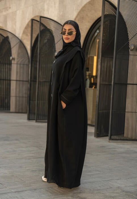 Woman wearing black Chinese-style abaya with structured collar and button-down front standing outdoors