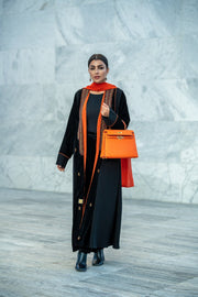 Black velvet abaya with vibrant orange accents, hand embroidery, and contrast piping worn with matching orange scarf and handbag.