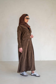 Woman wearing a brown velvet corduroy abaya with buttons and false pockets standing against a plain background
