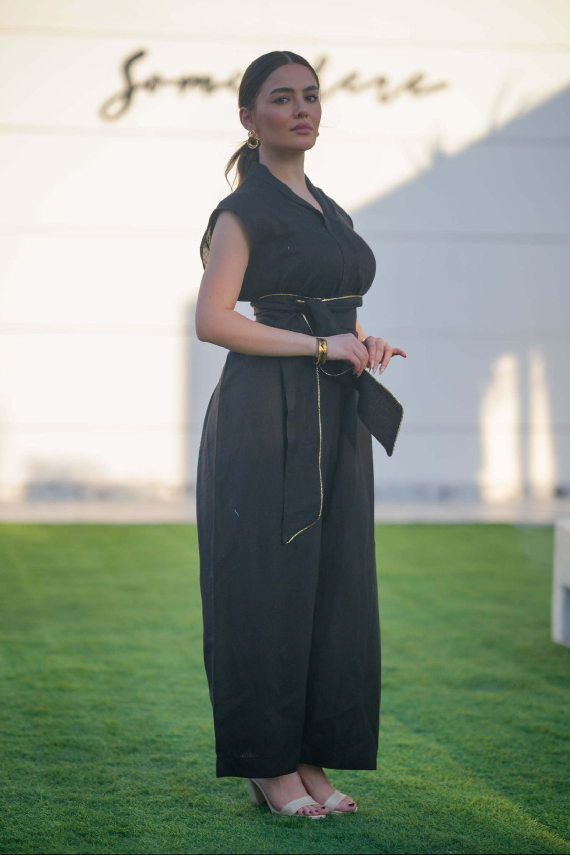 Woman wearing a sleek black linen jumpsuit with a cinched waist and wide-leg cut standing outdoors on grass.
