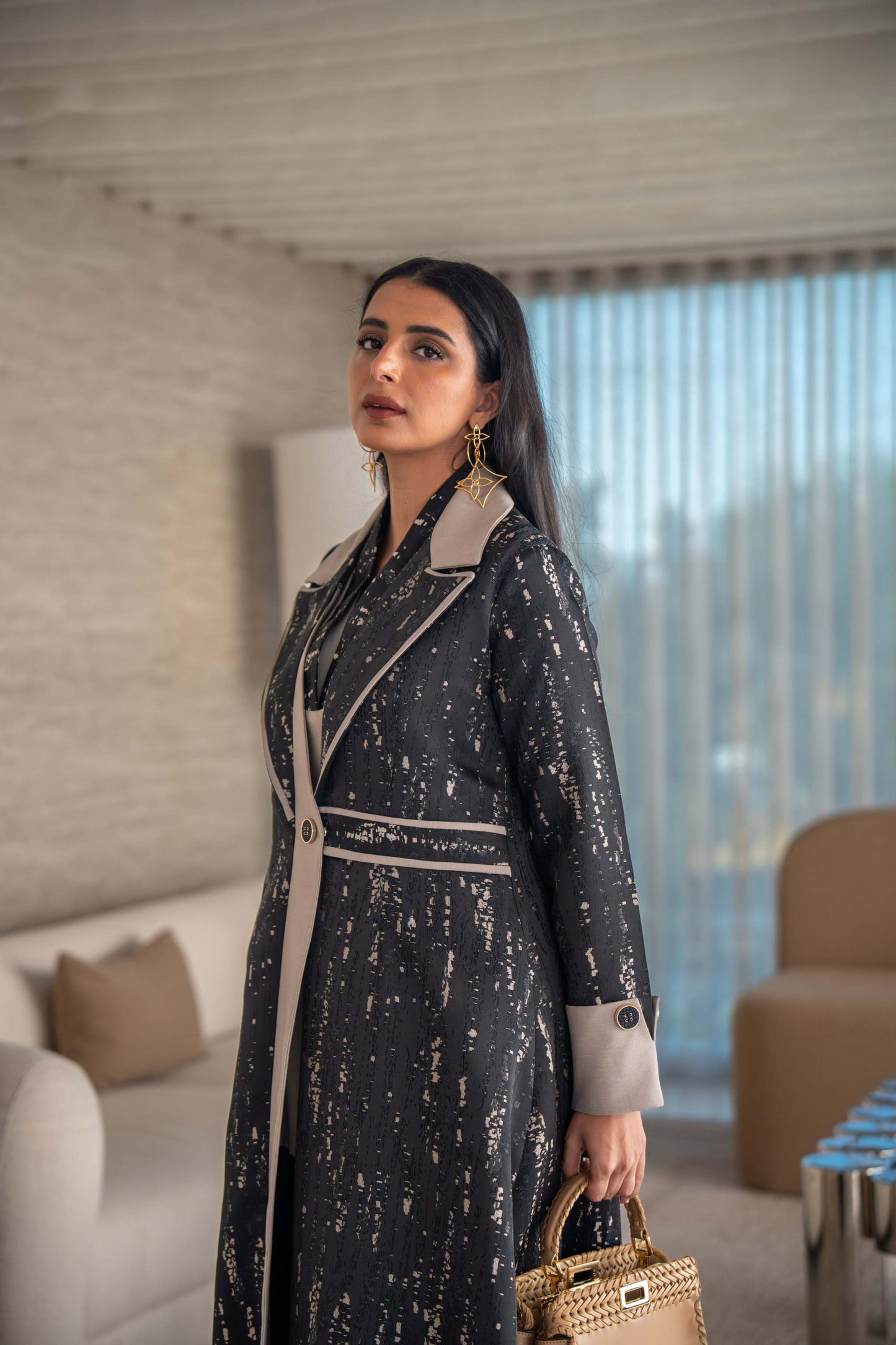 woman wearing elegant black and beige patterned Ashira abaya holding tan handbag in modern living room