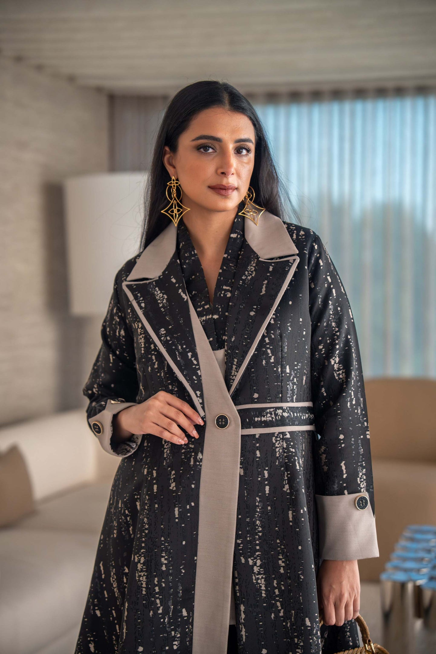 woman wearing elegant black and beige patterned Ashira abaya holding tan handbag in modern living room