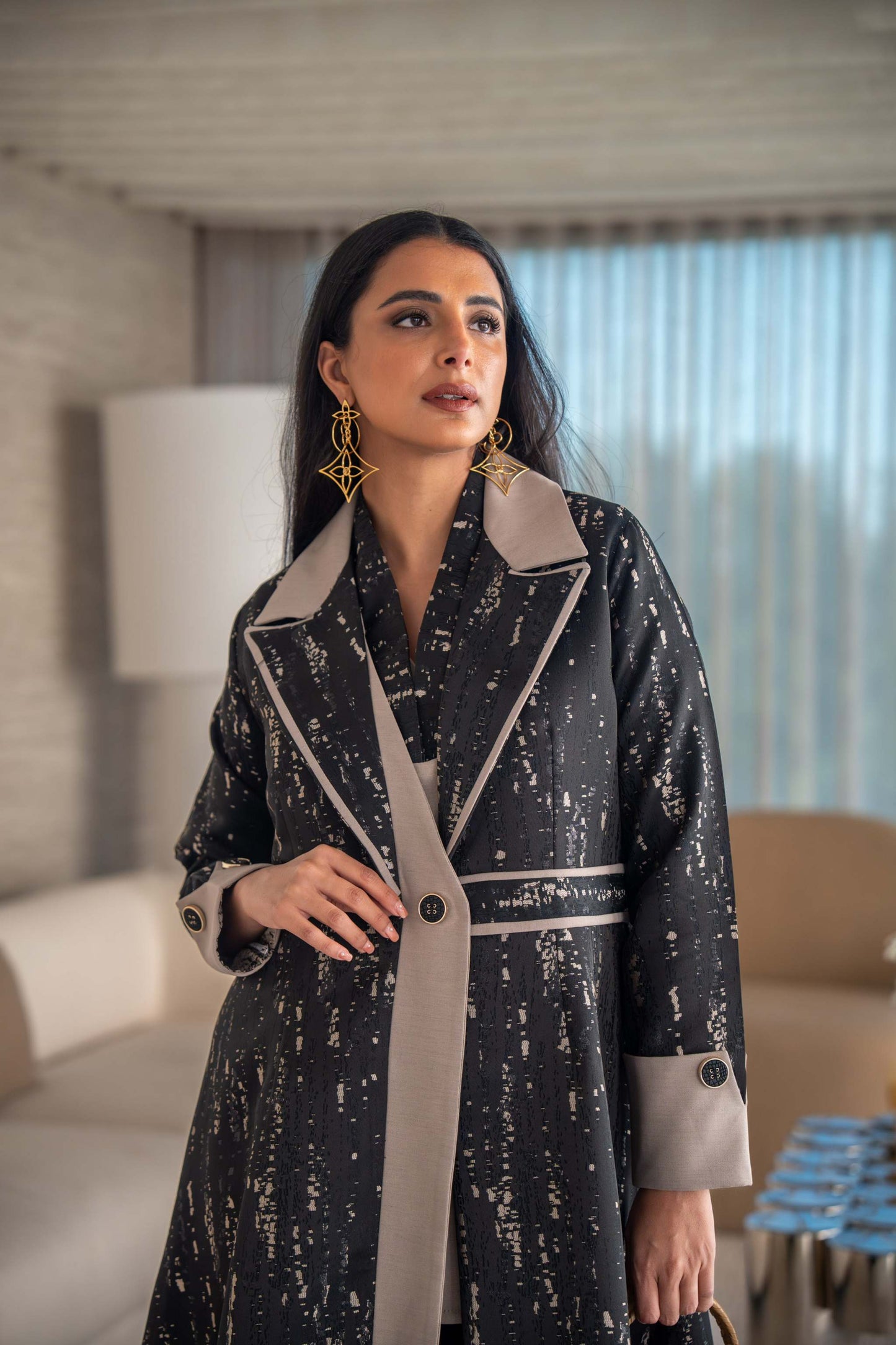 woman wearing elegant black and beige patterned Ashira abaya holding tan handbag in modern living room