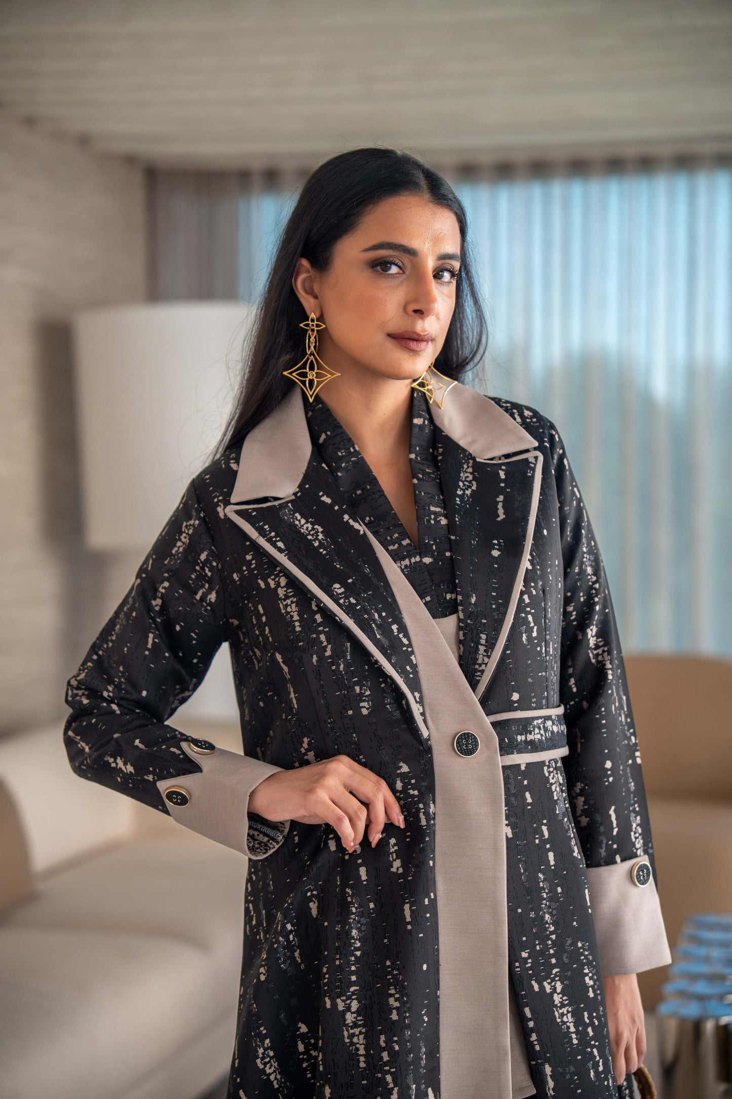 woman wearing elegant black and beige patterned Ashira abaya holding tan handbag in modern living room
