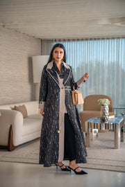 woman wearing elegant black and beige patterned Ashira abaya holding tan handbag in modern living room