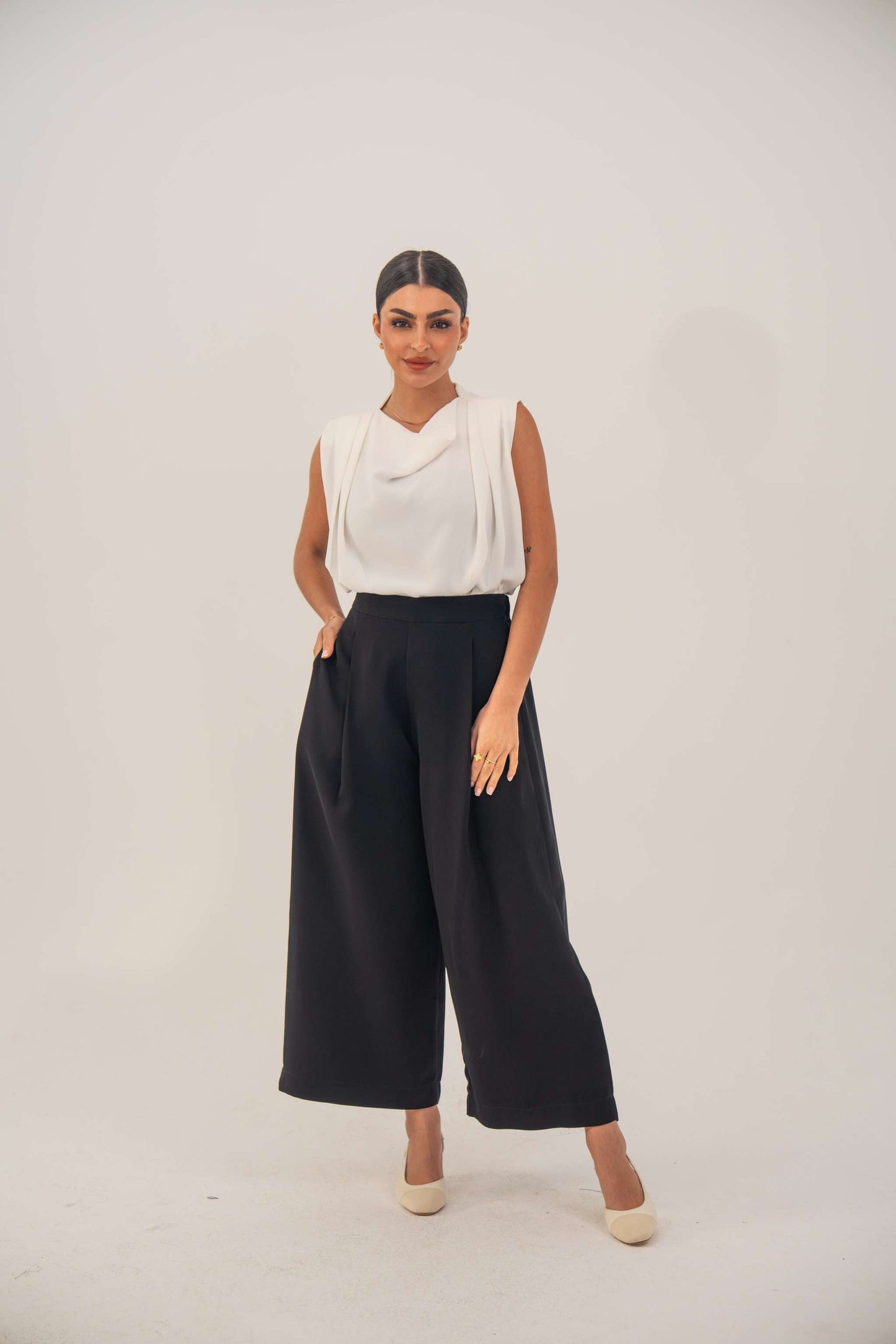 Woman wearing black crepe pants with a tailored fit and white sleeveless top standing against a plain background