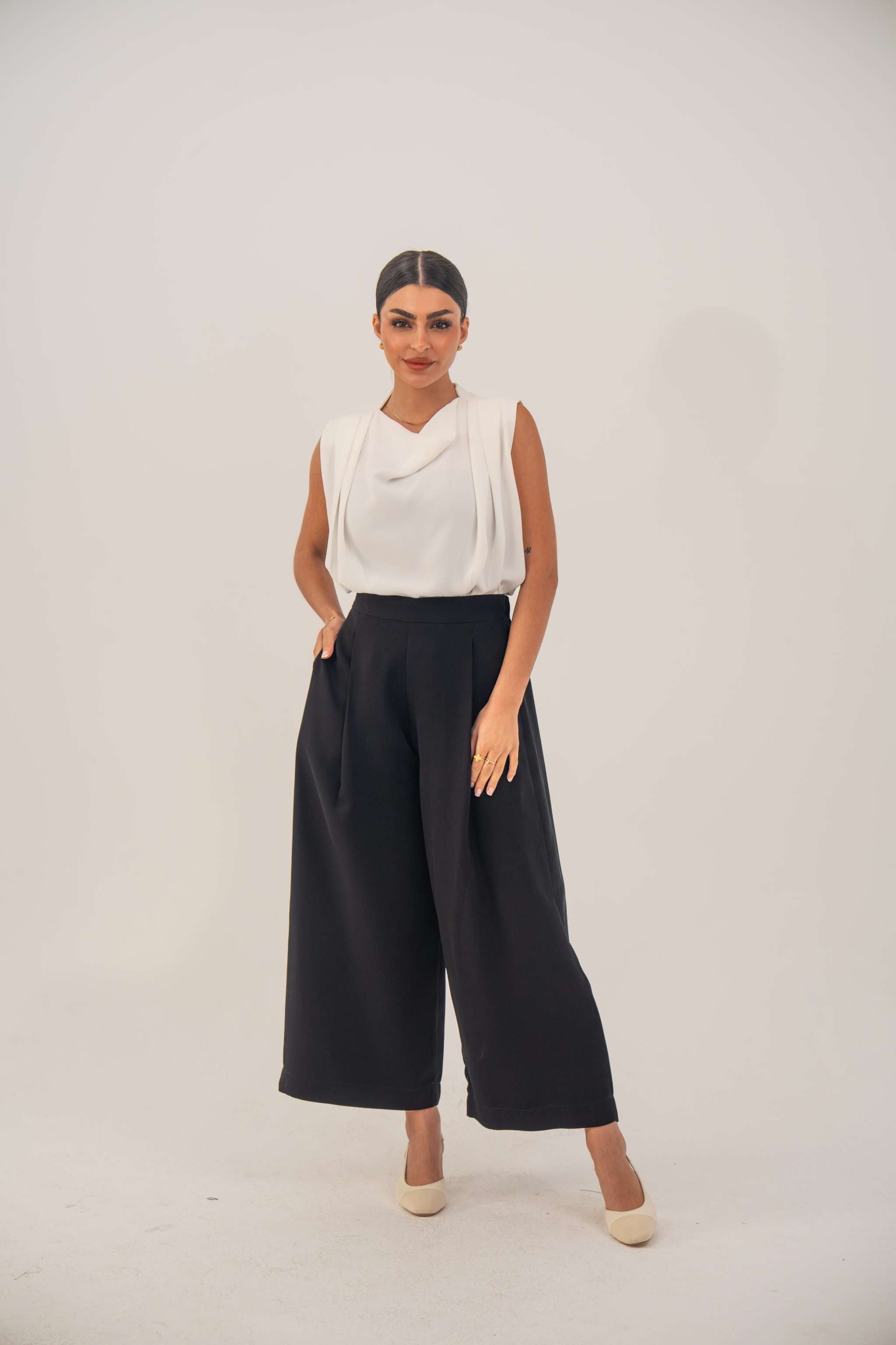 Woman wearing black crepe pants with a tailored fit and white sleeveless top standing against a plain background