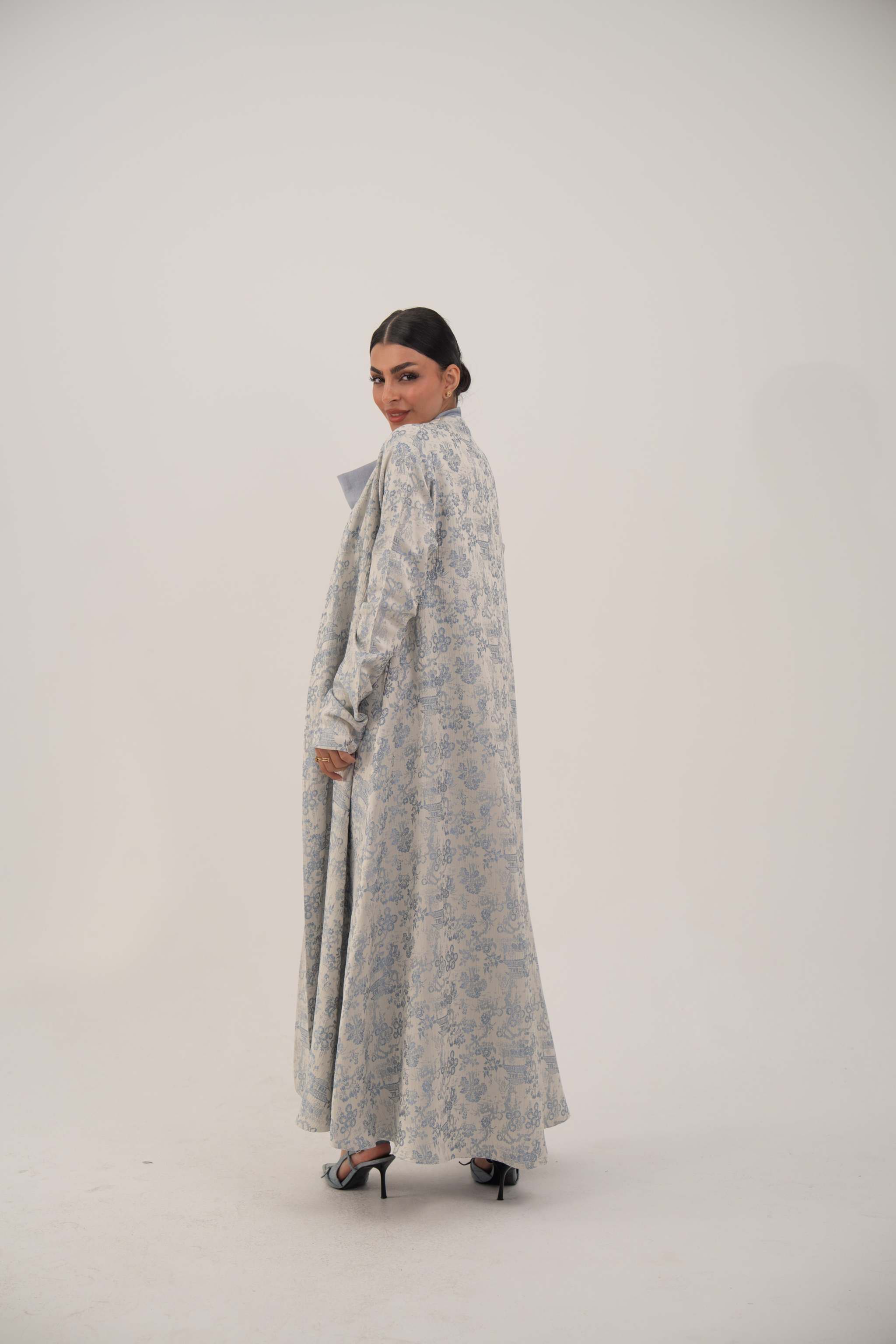 Woman wearing a long open-front jacquard silk abaya with a soft elegant pattern and simple lapel, styled with heels.