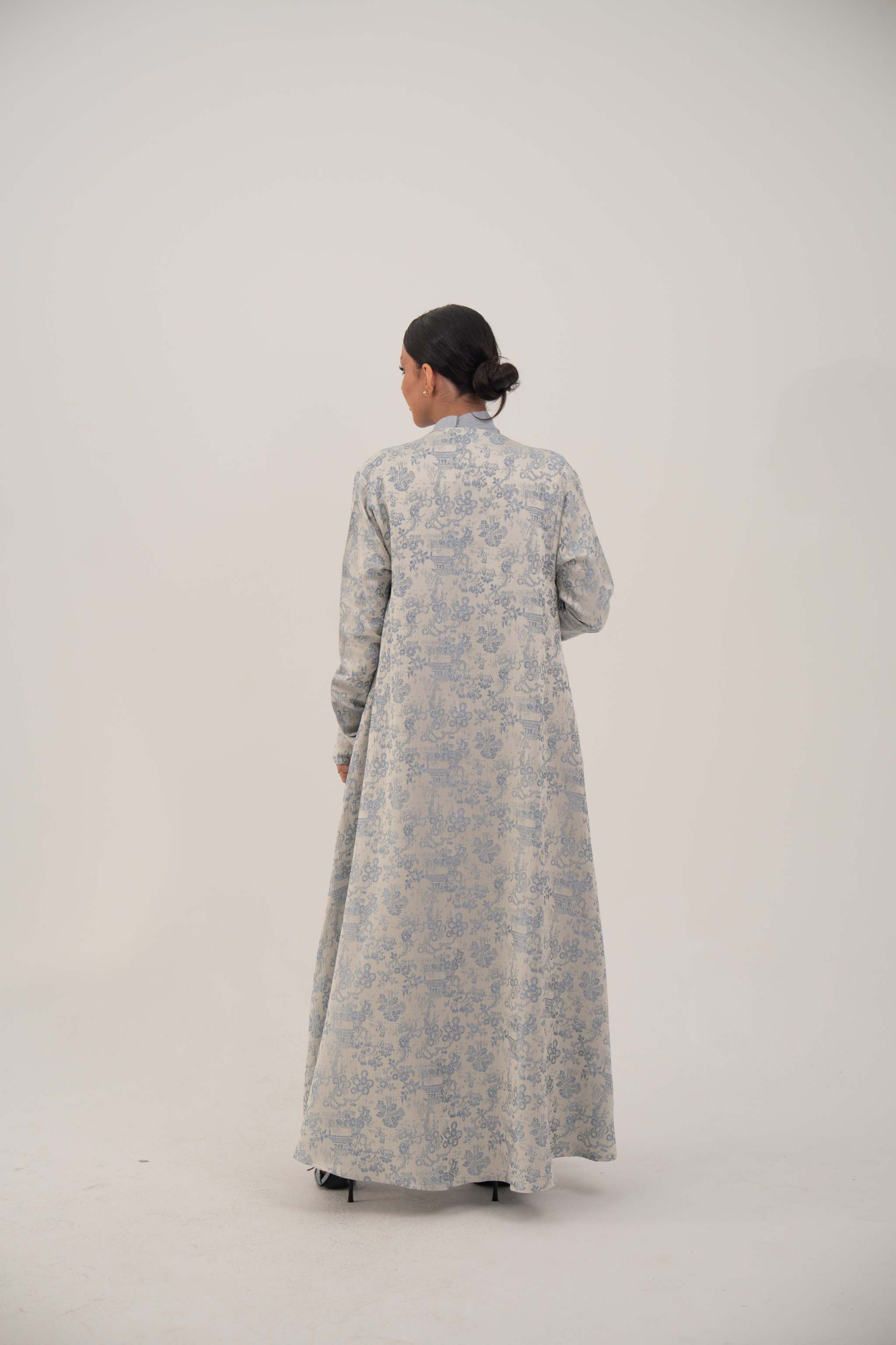 Back view of a woman wearing a long open-front jacquard silk abaya with a soft elegant pattern, simple lapel, and loose sleeves.