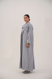 Woman wearing a lightweight blueish gray modern blazer-style abaya with wide lapel and embellished white bead and crystal cuffs