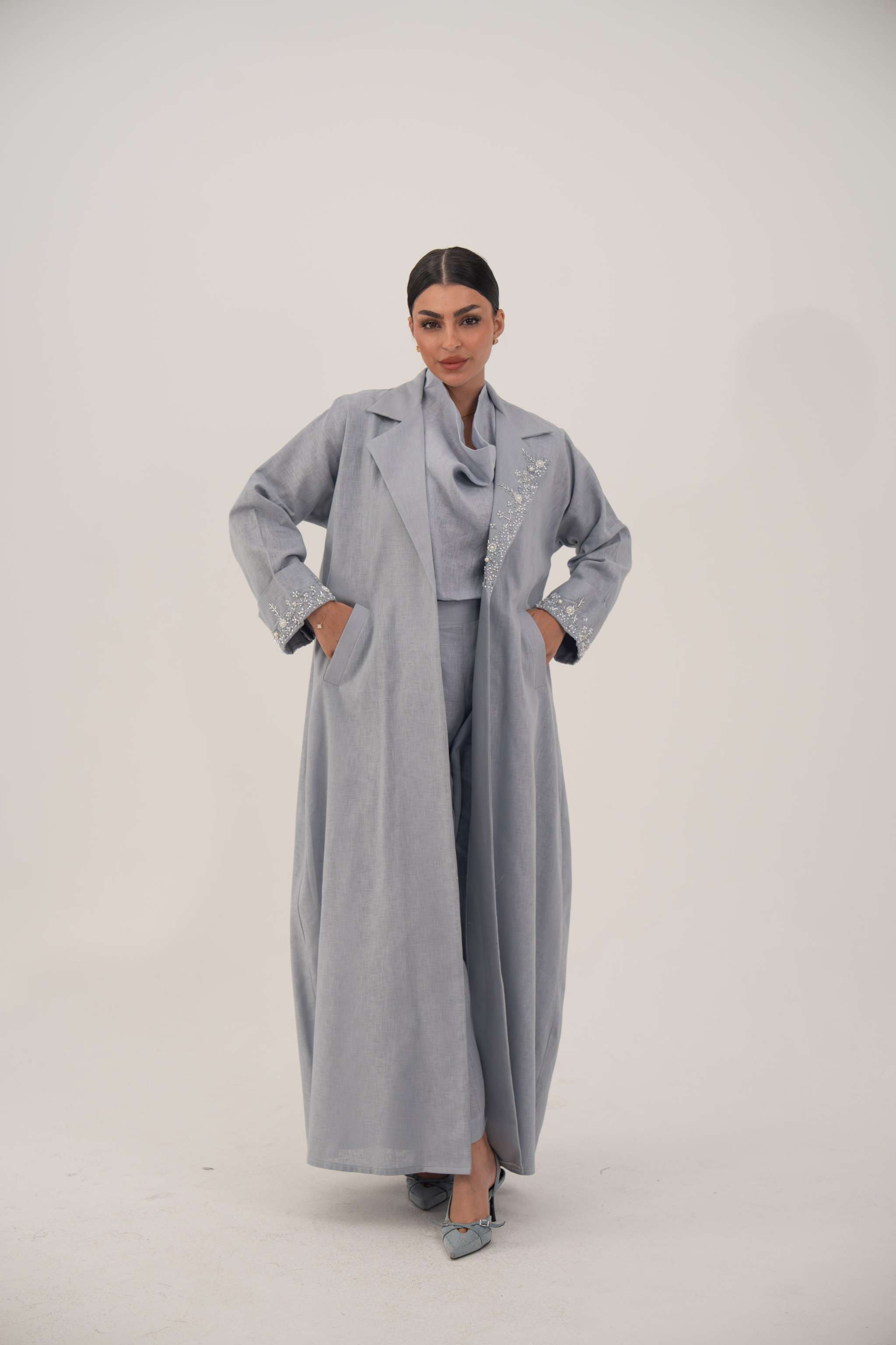 Woman wearing a modern blueish gray blazer abaya with lightweight breathable fabric and embellished lapel and cuffs.