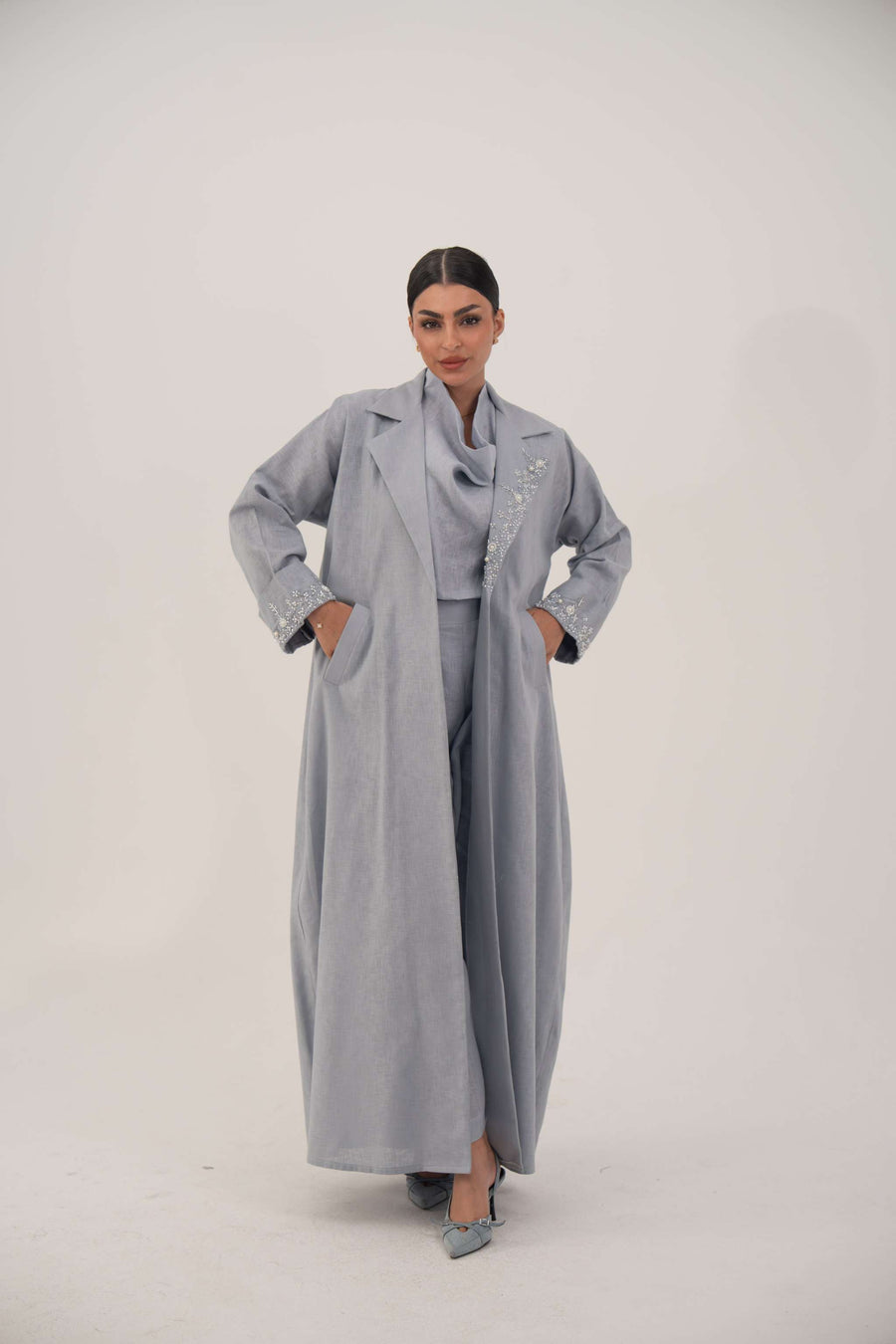Woman wearing a modern blueish gray blazer abaya with lightweight breathable fabric and embellished lapel and cuffs.