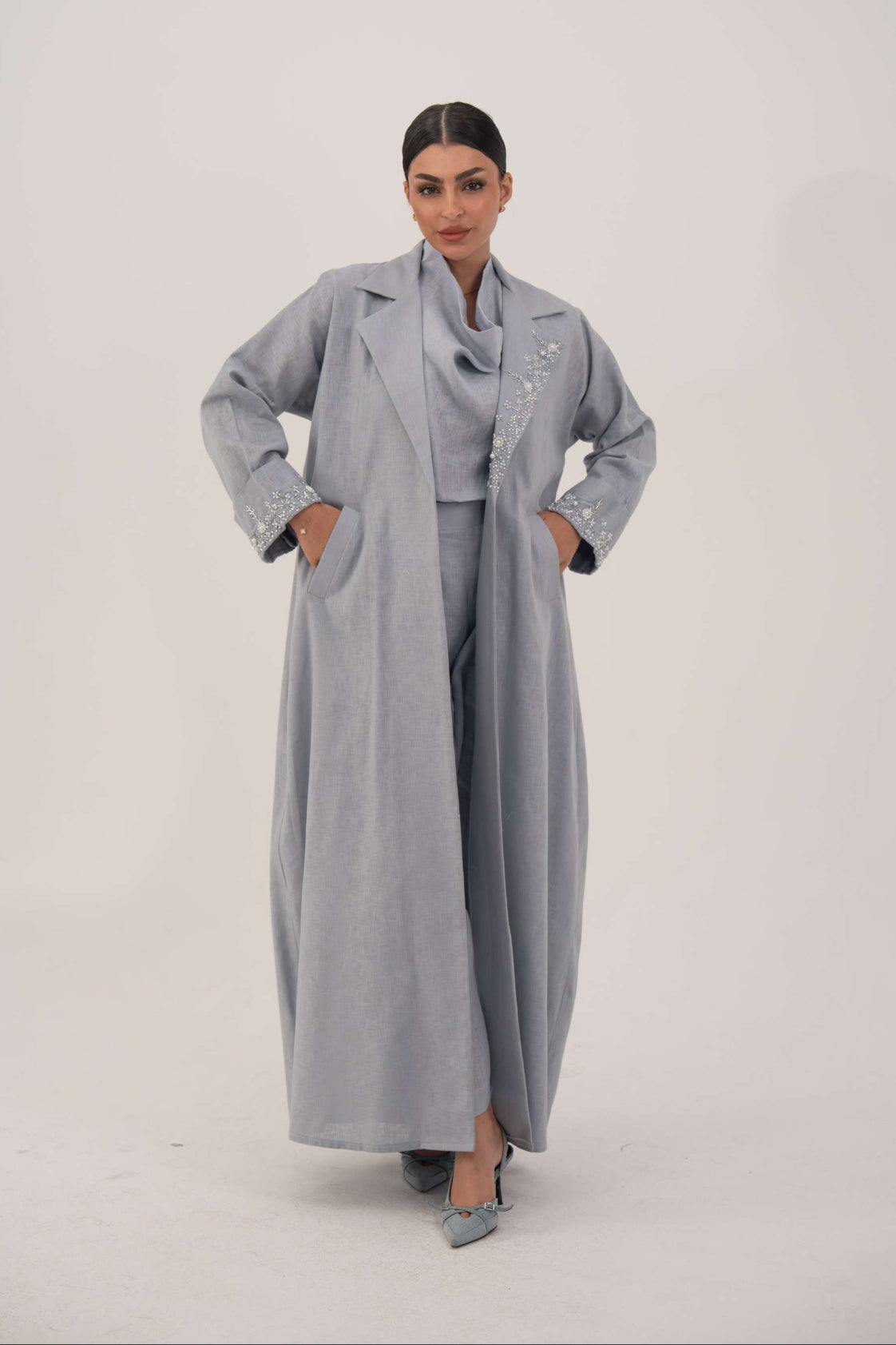 Woman wearing a modern blueish gray blazer abaya with lightweight breathable fabric and embellished lapel and cuffs.