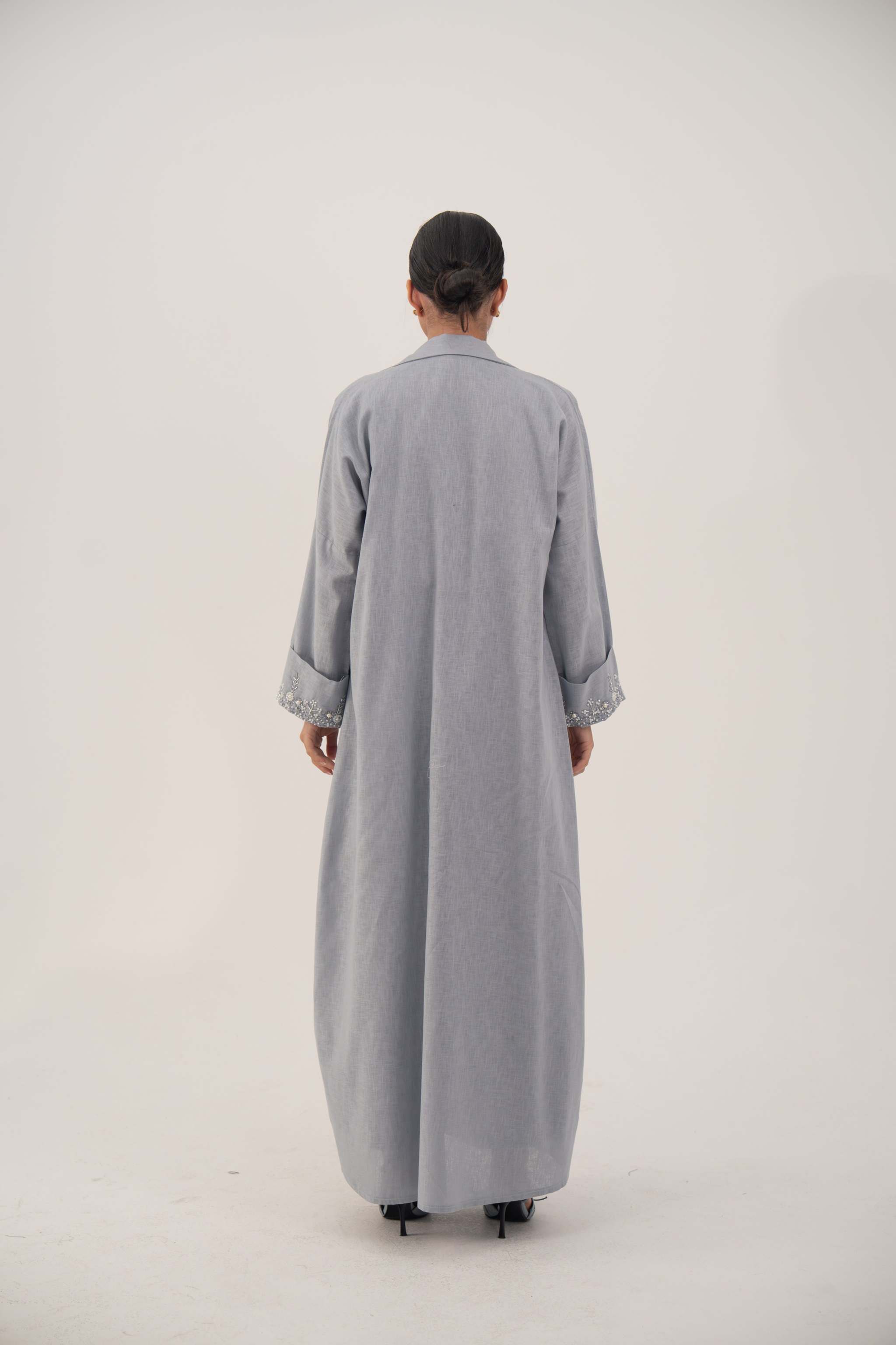 Back view of a lightweight blueish gray long abaya blazer with wide embellished cuffs and a modern straight-cut design