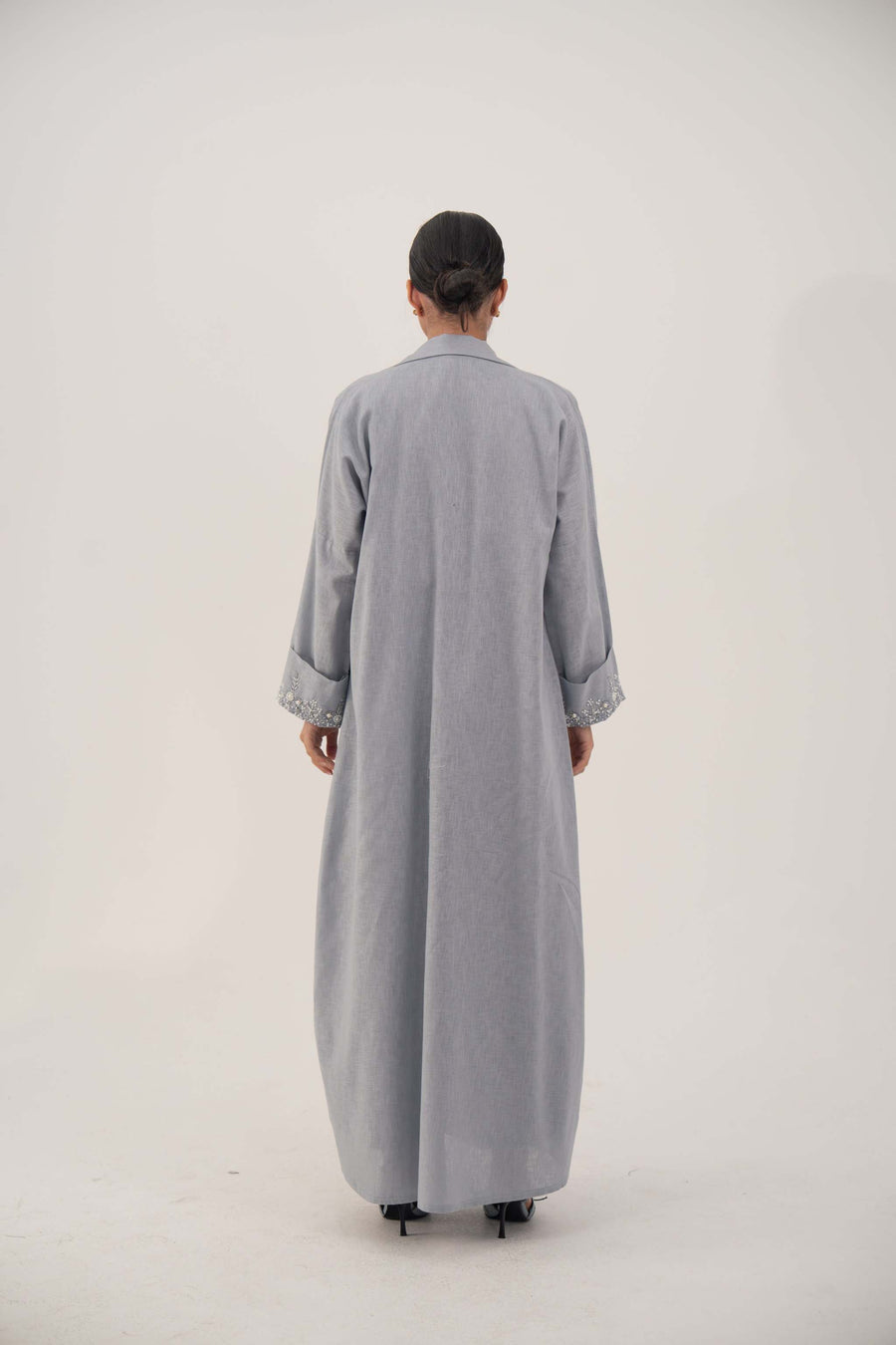 Back view of a lightweight blueish gray long abaya blazer with wide embellished cuffs and a modern straight-cut design