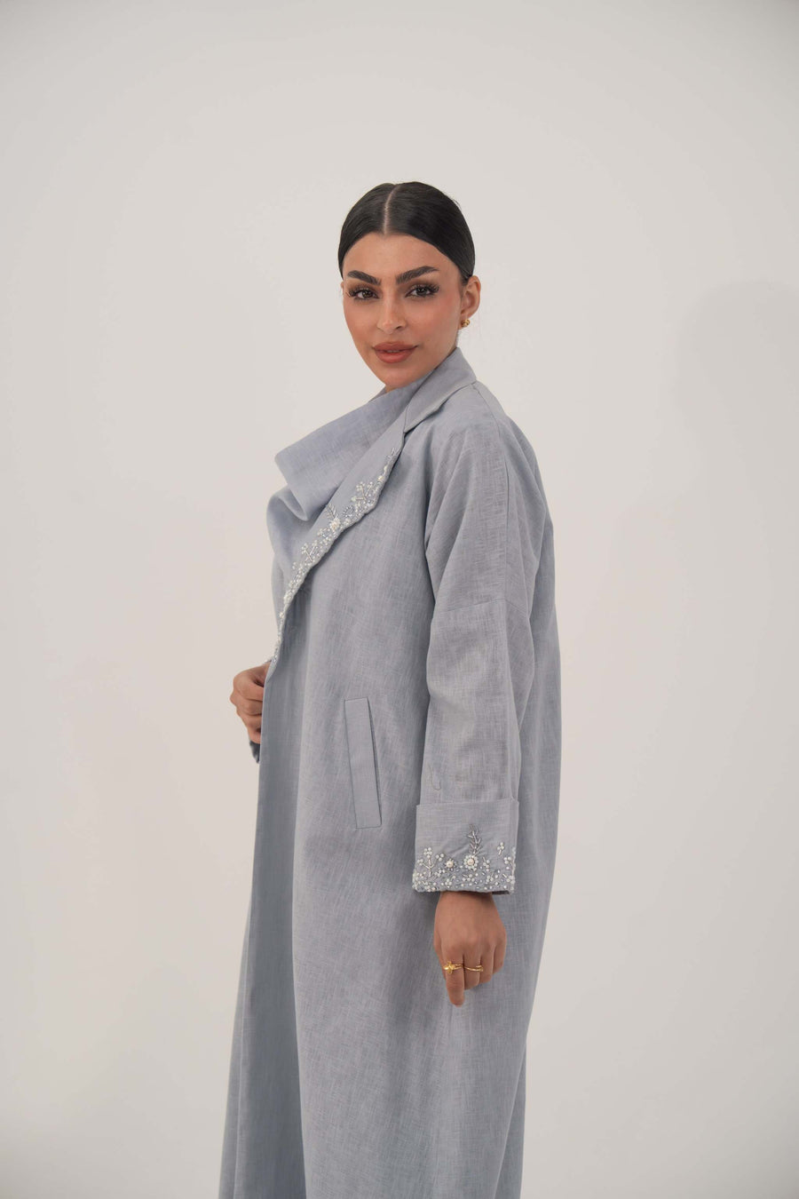 Woman wearing a soft blueish gray lightweight blazer-style abaya with wide open lapel and embellished pearl and crystal cuffs