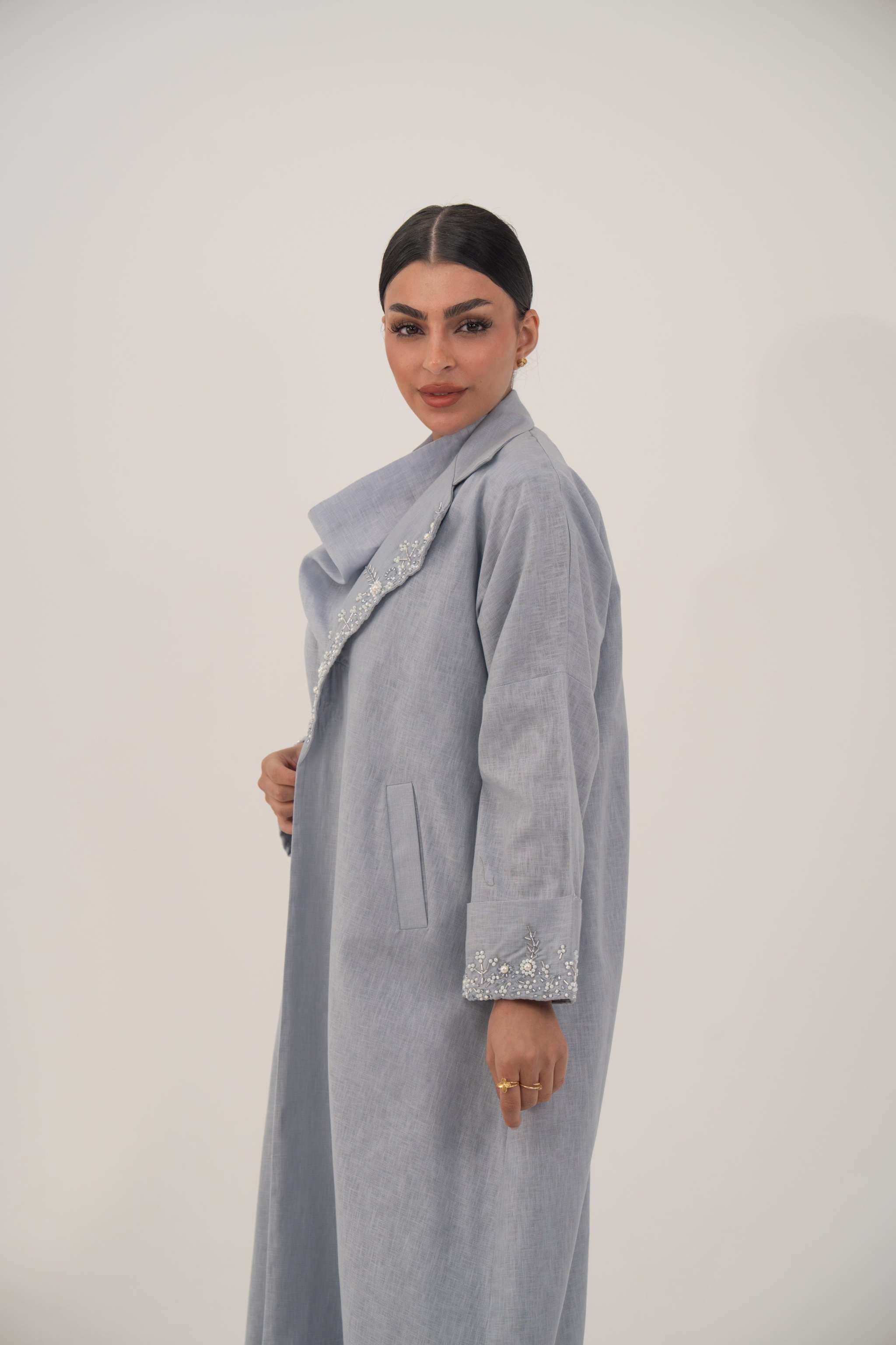 Woman wearing a soft blueish gray lightweight blazer-style abaya with wide open lapel and embellished pearl and crystal cuffs