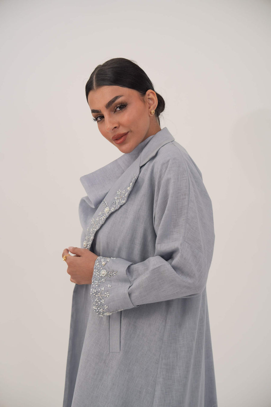 Woman wearing a lightweight blueish gray blazer-style abaya with wide lapel and embellished white bead and crystal details on lapel and cuffs