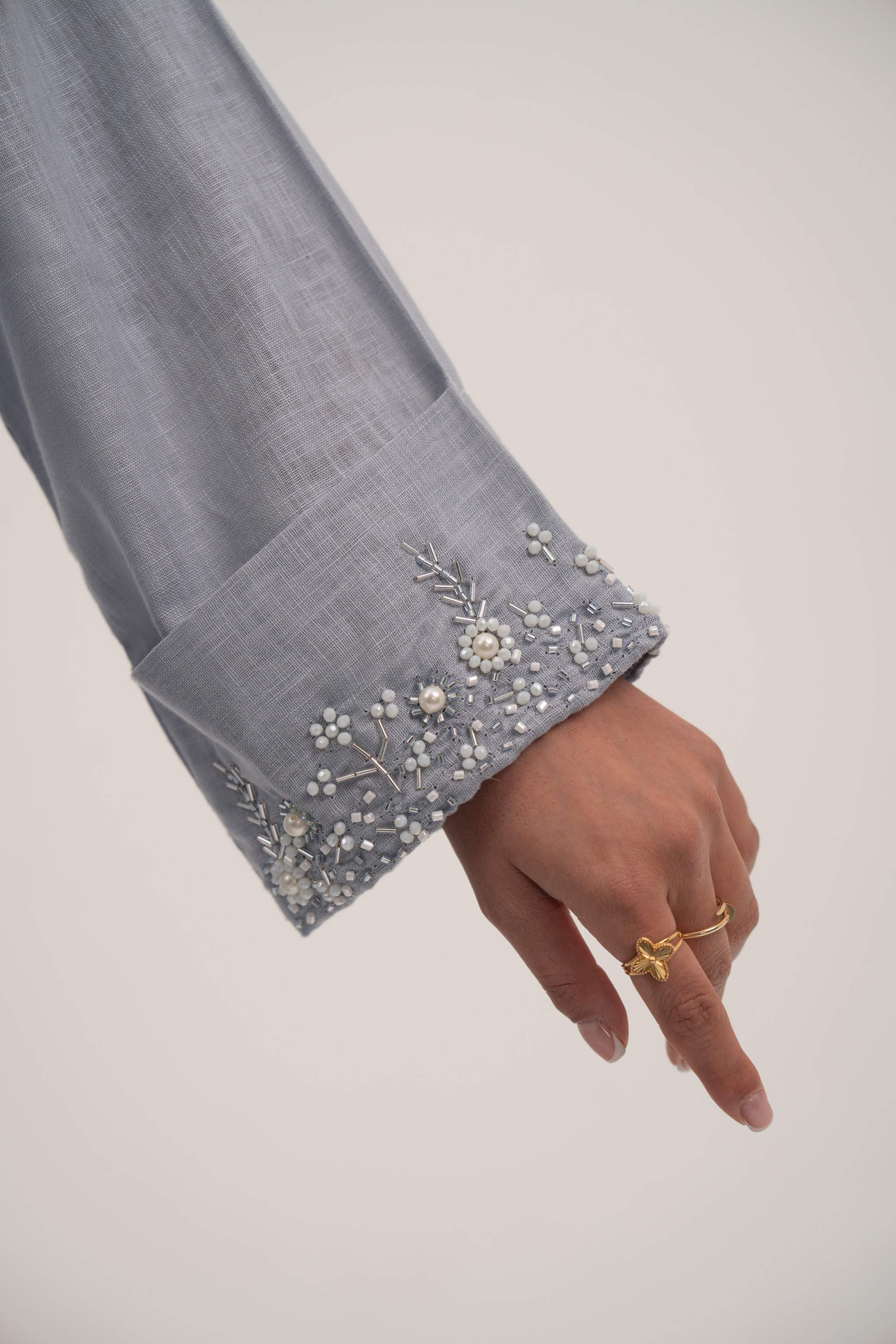 Close-up of soft blueish gray blazer sleeve with delicate white bead and crystal embellishments on wide cuff