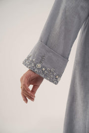 Close-up of a light blueish gray blazer sleeve with delicate white bead and crystal embellishments on the wide cuff.