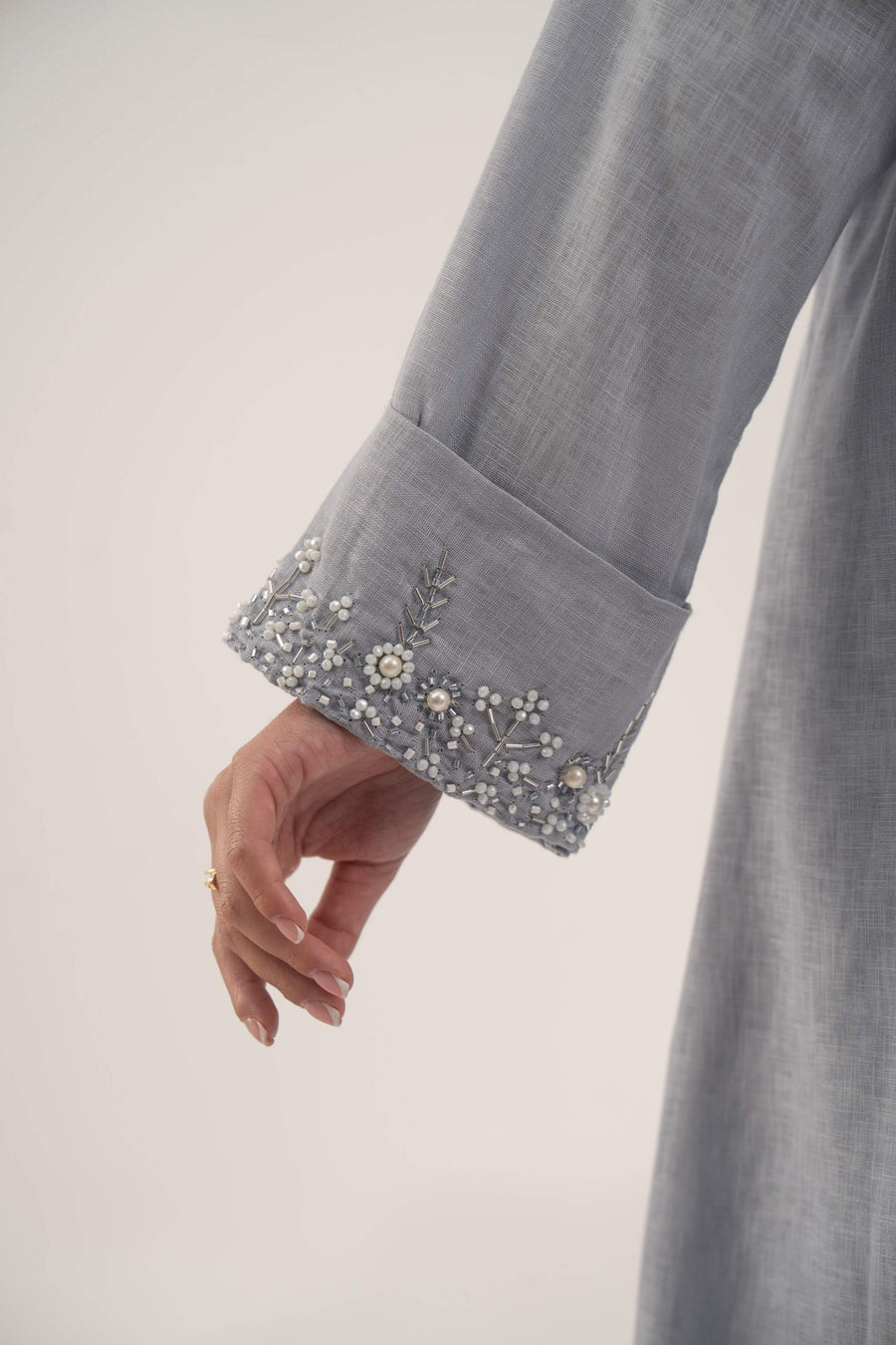 Close-up of a light blueish gray blazer sleeve with delicate white bead and crystal embellishments on the wide cuff.