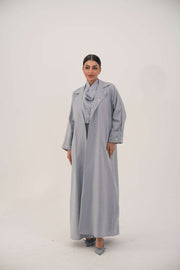Woman wearing a lightweight soft blueish gray modern blazer-style abaya with delicate white bead and crystal embellishments on the wide lapel and cuffs.