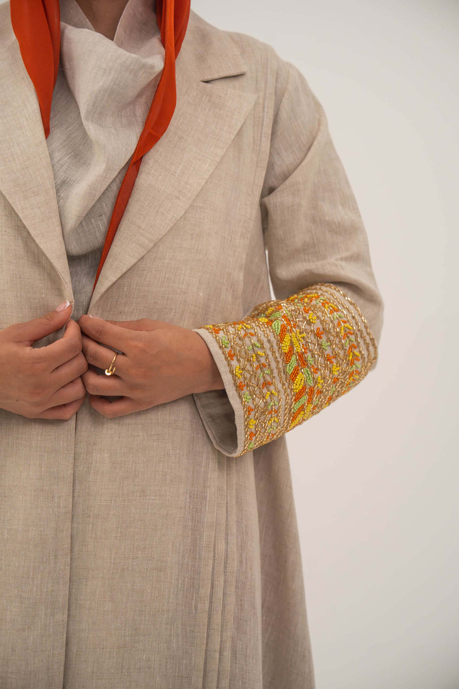 Beige linen blend abaya with wide lapels and vibrant orange, gold, and green shak embroidery on sleeves, featuring subtle orange chiffon lining - sophisticated abaya