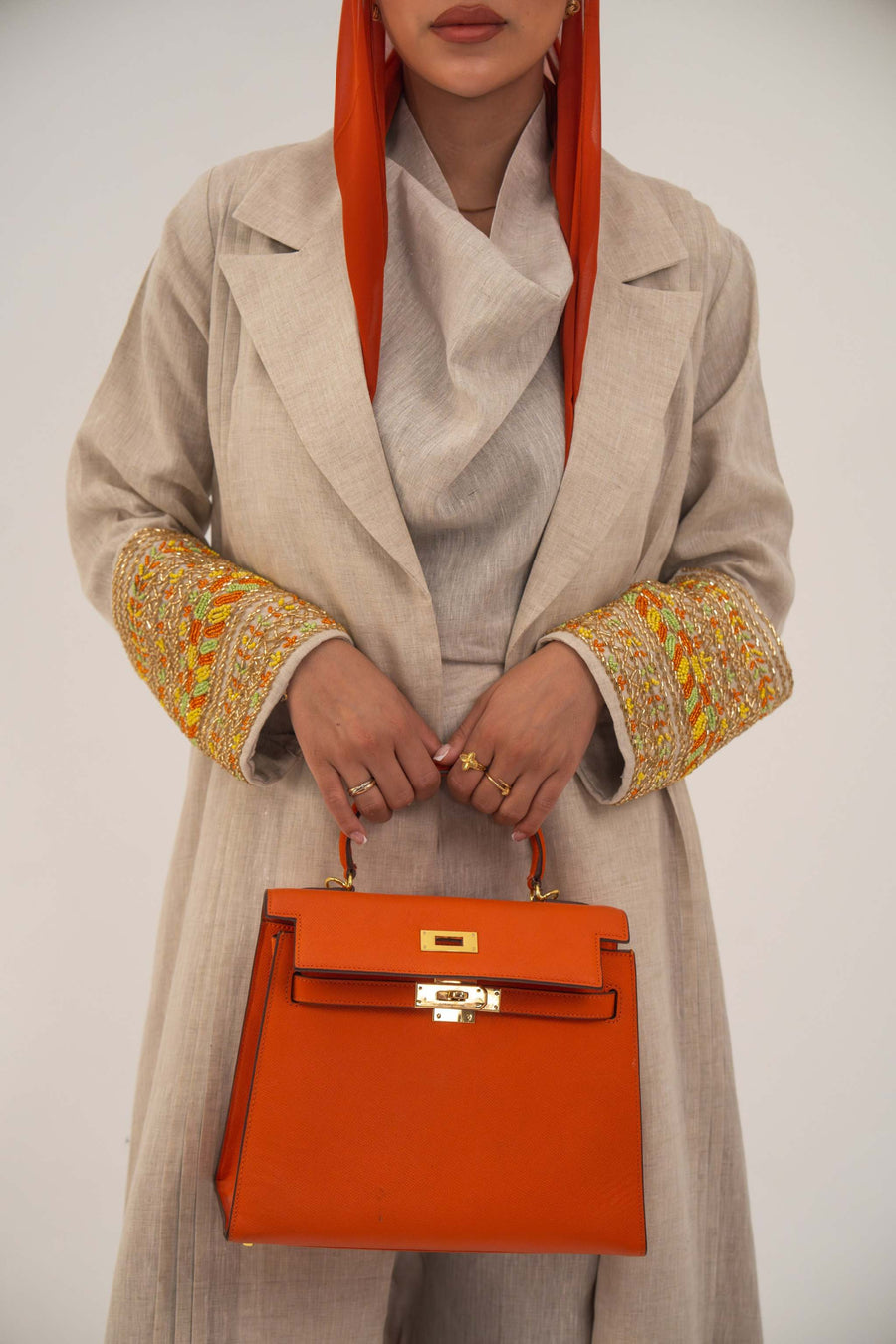 Beige linen abaya with tailored blazer cut and vibrant orange, gold, green embroidery on sleeves, paired with orange headscarf and handbag - sophisticated abaya