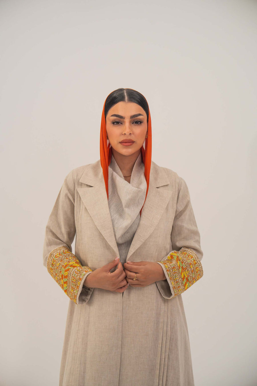 Beige linen blend abaya with blazer-style cut and vibrant orange, gold, and green embroidery on sleeves, paired with an orange headscarf -