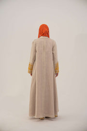 Back view of a beige linen blend abaya with wide lapels, orange, gold, and green embroidery on sleeves, and an orange chiffon inner lining, worn with an orange headscarf.-sophisticated abaya